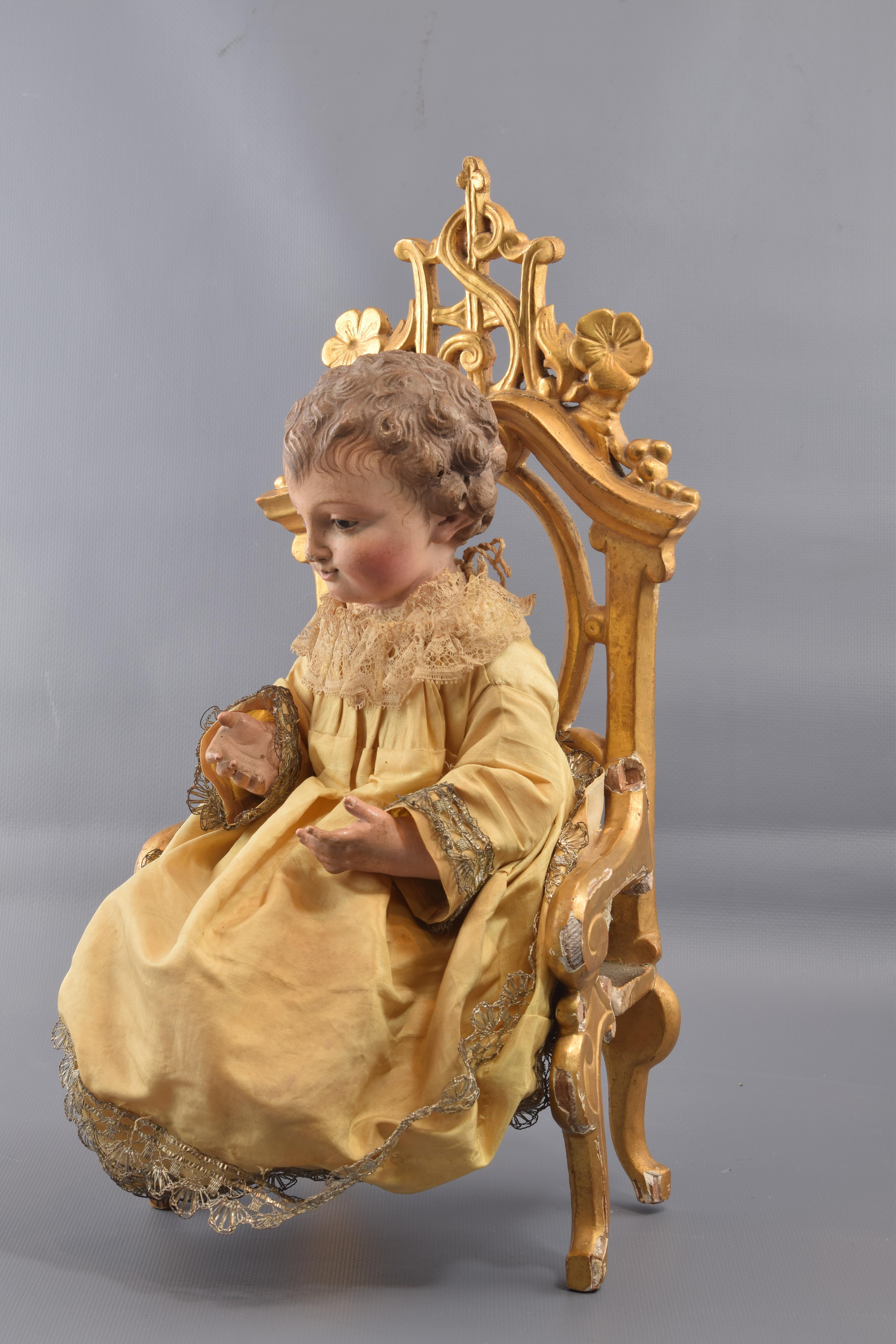 Child Jesus. Polychrome wood, giltwood, textile, metal, etc., Spain, 19th century
Baby Jesus dressed in carved and polychrome wood sitting on a high-backed throne (decorated with flowers, Classic shapes, cabriolet legs and flower pomp highlighting
