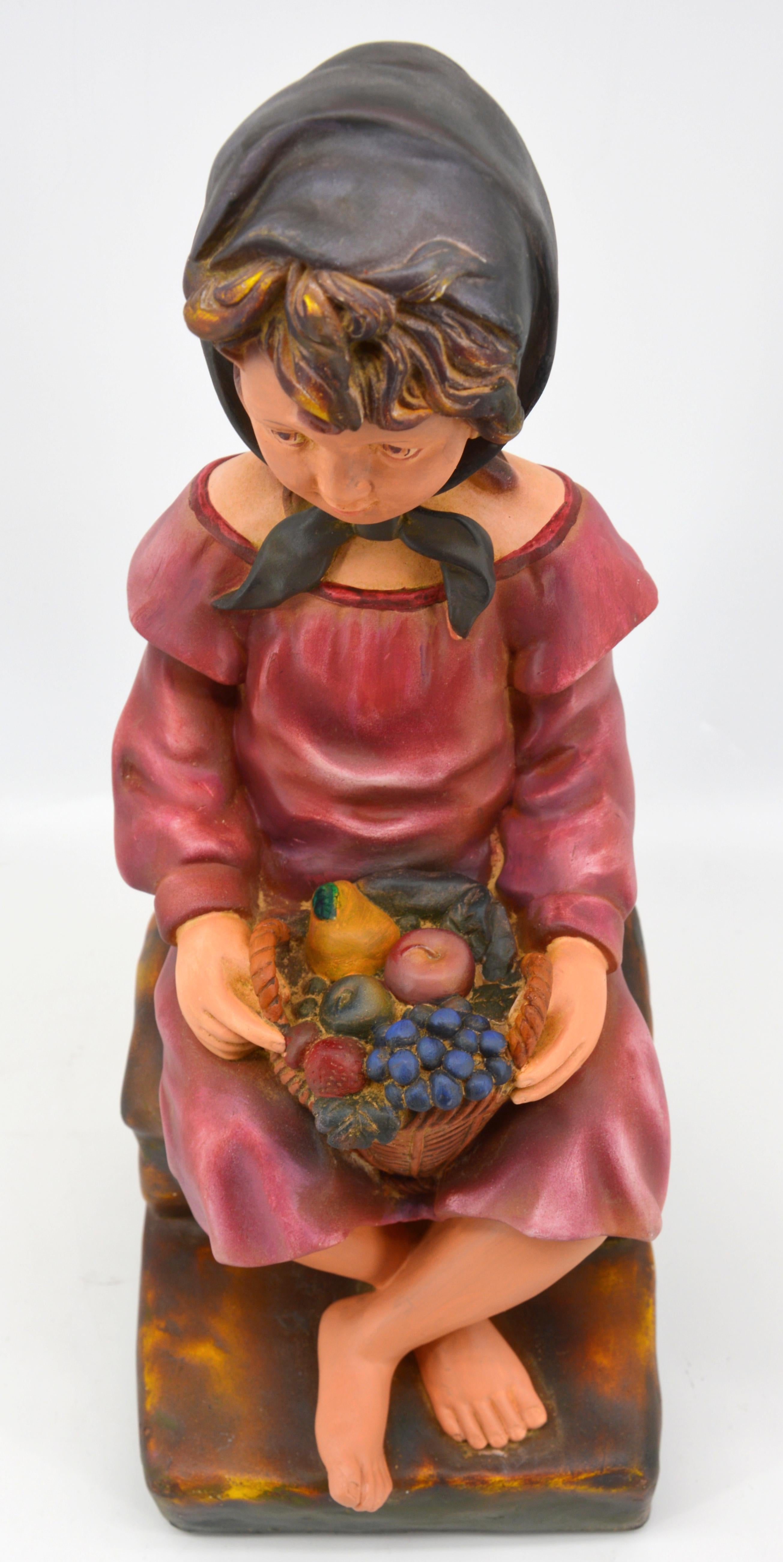 This charming sculpture, titled Child with a Fruit Basket, was crafted in France in the early 1900s and is a delightful representation of the period's artistry. Made from polychrome plaster, the sculpture portrays a young child holding a basket of
