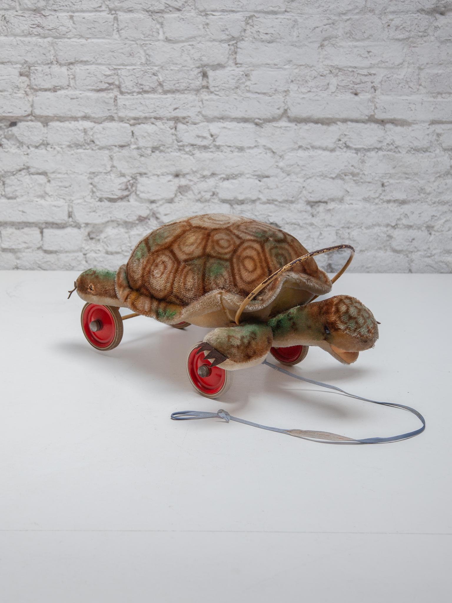 Jouet original à tirer et à asseoir en forme de tortue de Steiff, vers les années 1950. Il est équipé d'une corde de traction d'origine et de roues en caoutchouc d'origine avec des côtés peints en rouge ; la barre d'origine se trouve au-dessus du
