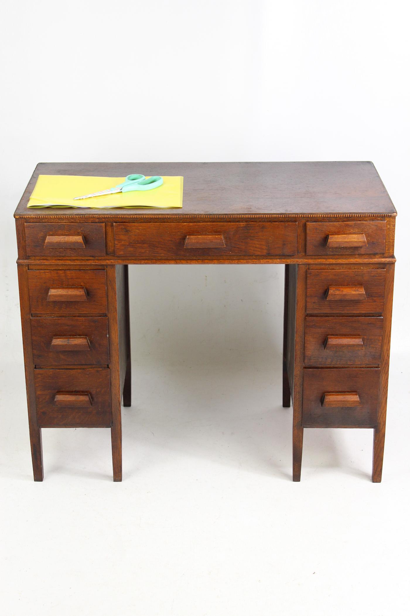 A charming and unusual vintage English art deco childs oak desk dating from circa 1930s. With a central drawer flanked by a bank of 4 graduated drawers, each fitted with a triangular handles. With panelled back and sides the top with beaded edging