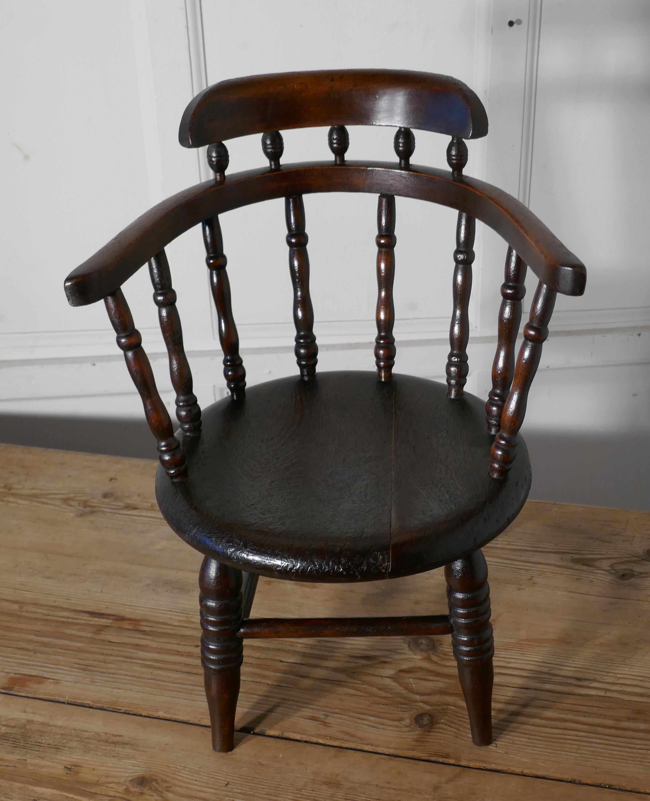 Childs chair, in the style of a Captain’s chair

This is a very unusual child’s chair, the chair has a rounded spindle back with which curves around to form the arms in the style of a smokers bow or Captains chair with a thick round elm seat
This