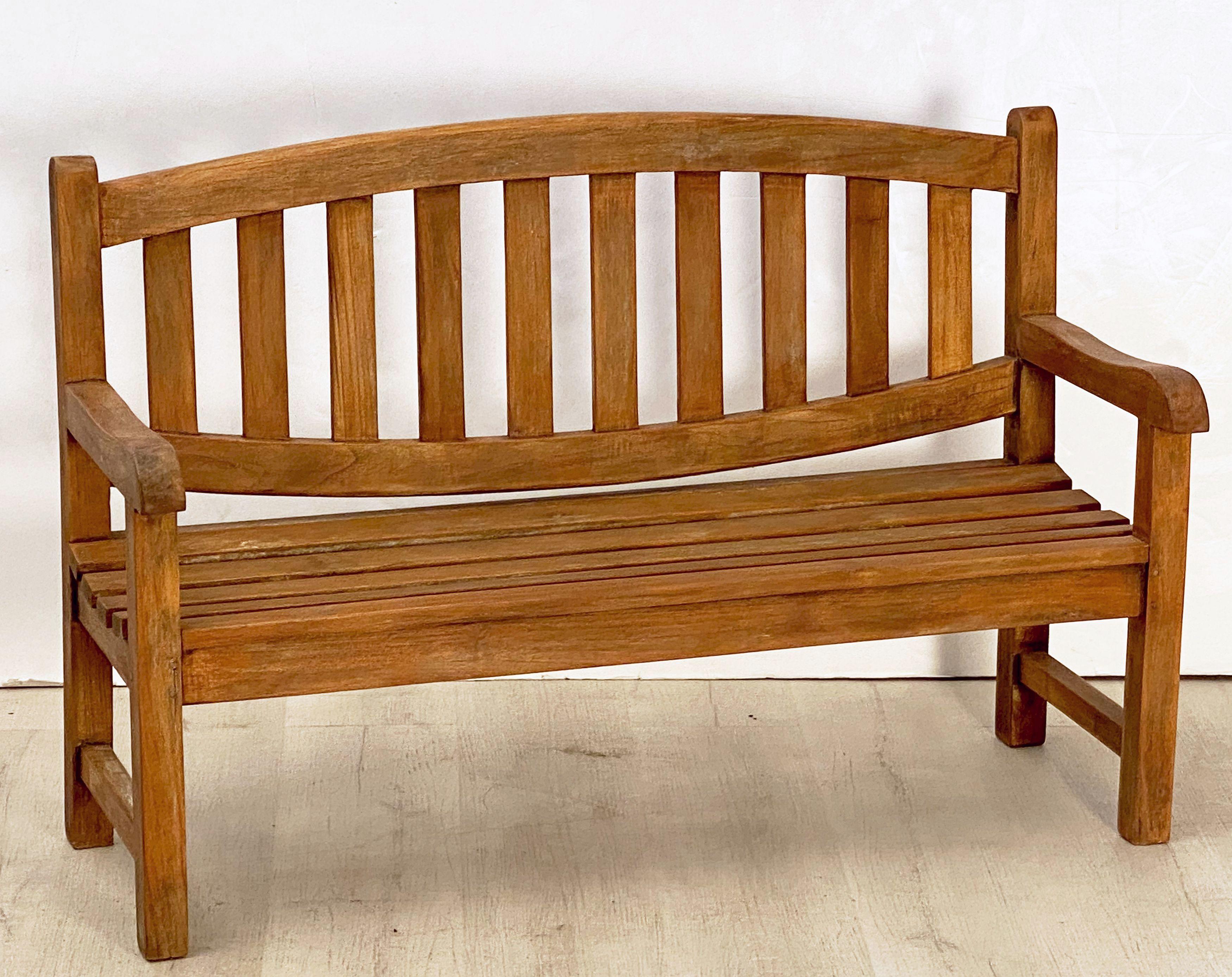 A fine English child's garden bench or seat of patinated teak featuring a slatted back with shaped arms over a comfortable seat, and resting on four legs.