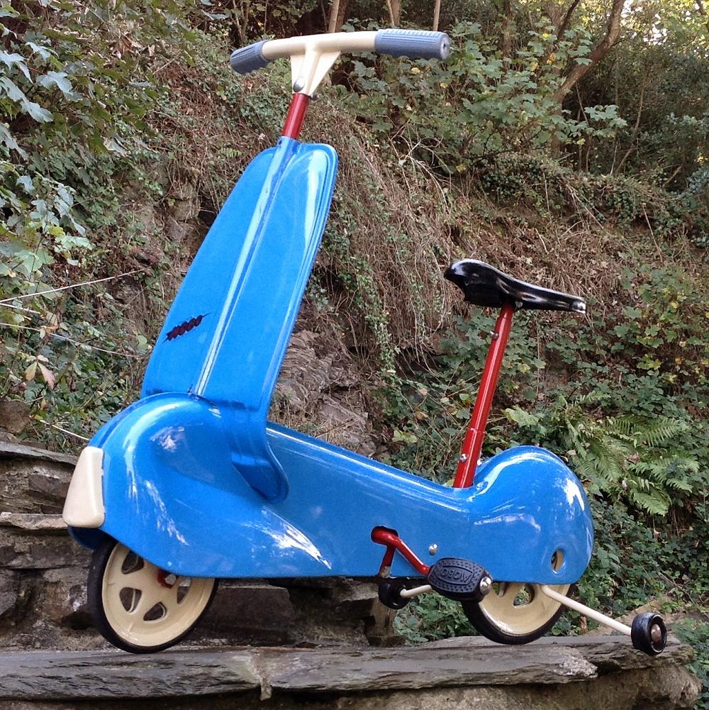 The Mobo Scootabike (also called a Scoot-a-Bike) was first introduced in 1959. For those of a certain generation, a Mobo scooter would have been their first ride as a child. Chain drive, rubber-wheeled outriders, elegantly contoured streamline