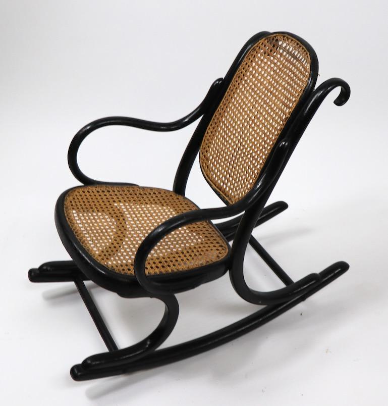 Childs rocking chair by Thonet. This example is in good overall condition, it shows some minor loss to base of backrest panel. Frame. Black finish frame, with caned seat and back. Measures: Seat H 12 x arm H 16 inch.