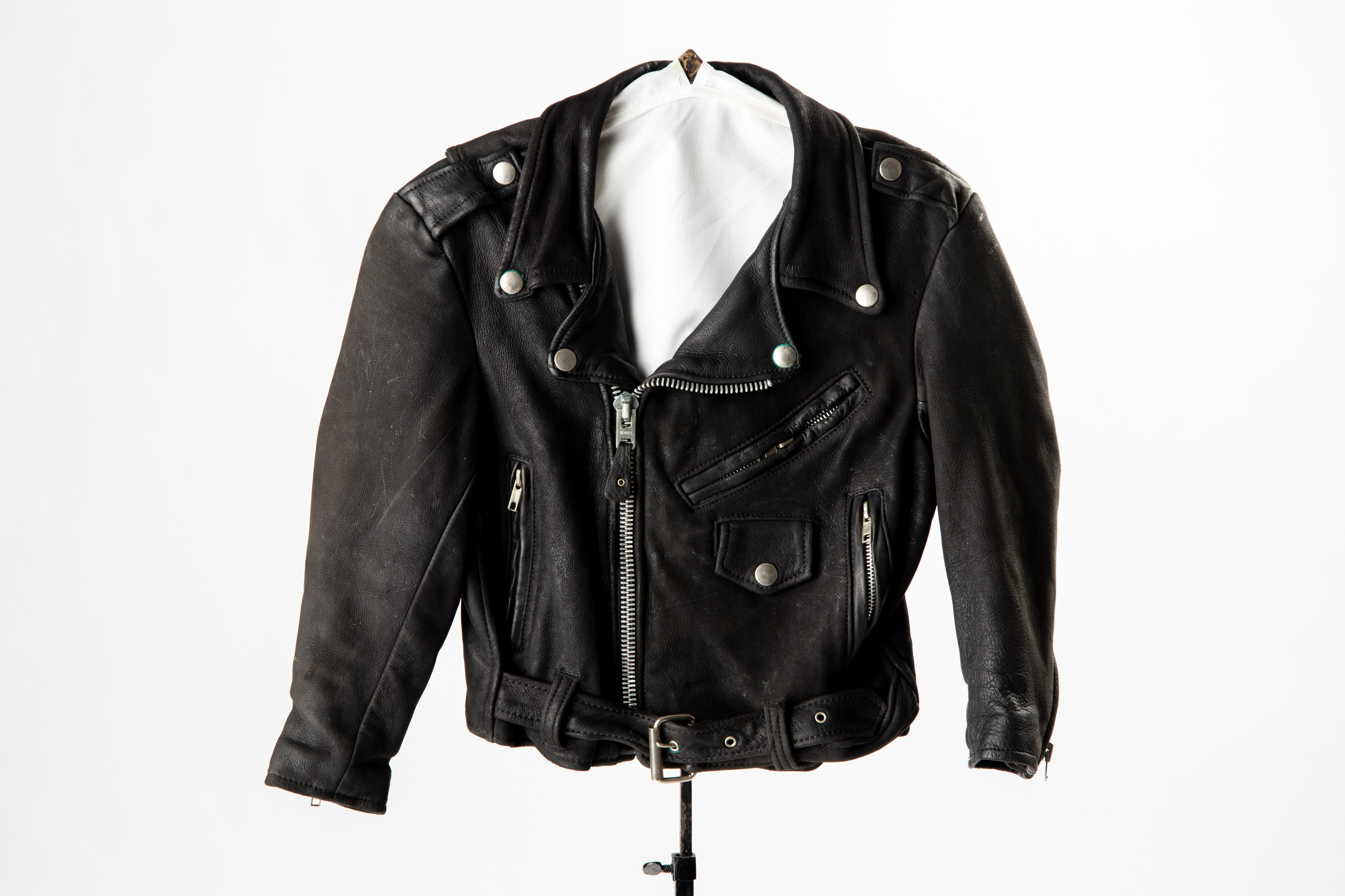 Veste de moto vintage en cuir noir pour enfant, taille 8. 
Les détails authentiques sont la fermeture à glissière sur le devant, les poignets et les poches latérales zippés, le col et la poche avant à boutons-pression en métal. La ceinture en cuir à
