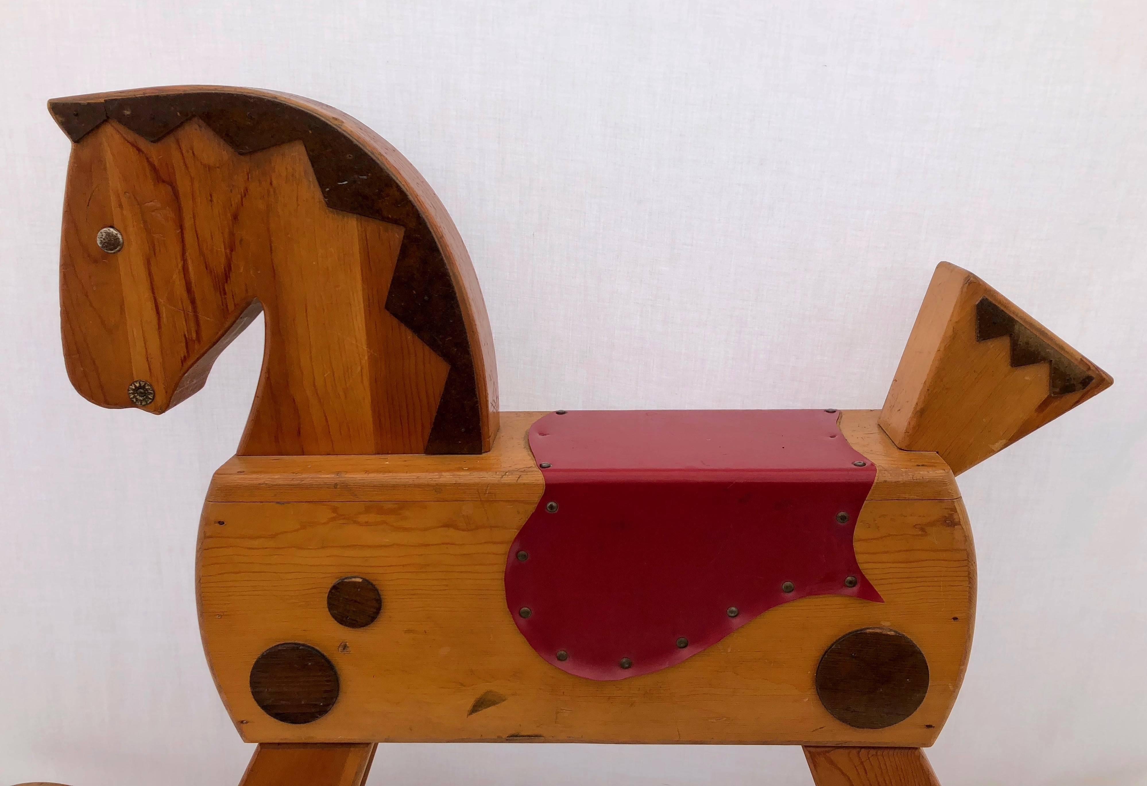 This is an absolutely charming child's wooden rocking horse with a great patina, pull-out foot rests, a mane in carved wood and saddle in red material with eyes and wood accents. Any child would love to ride such a pony.