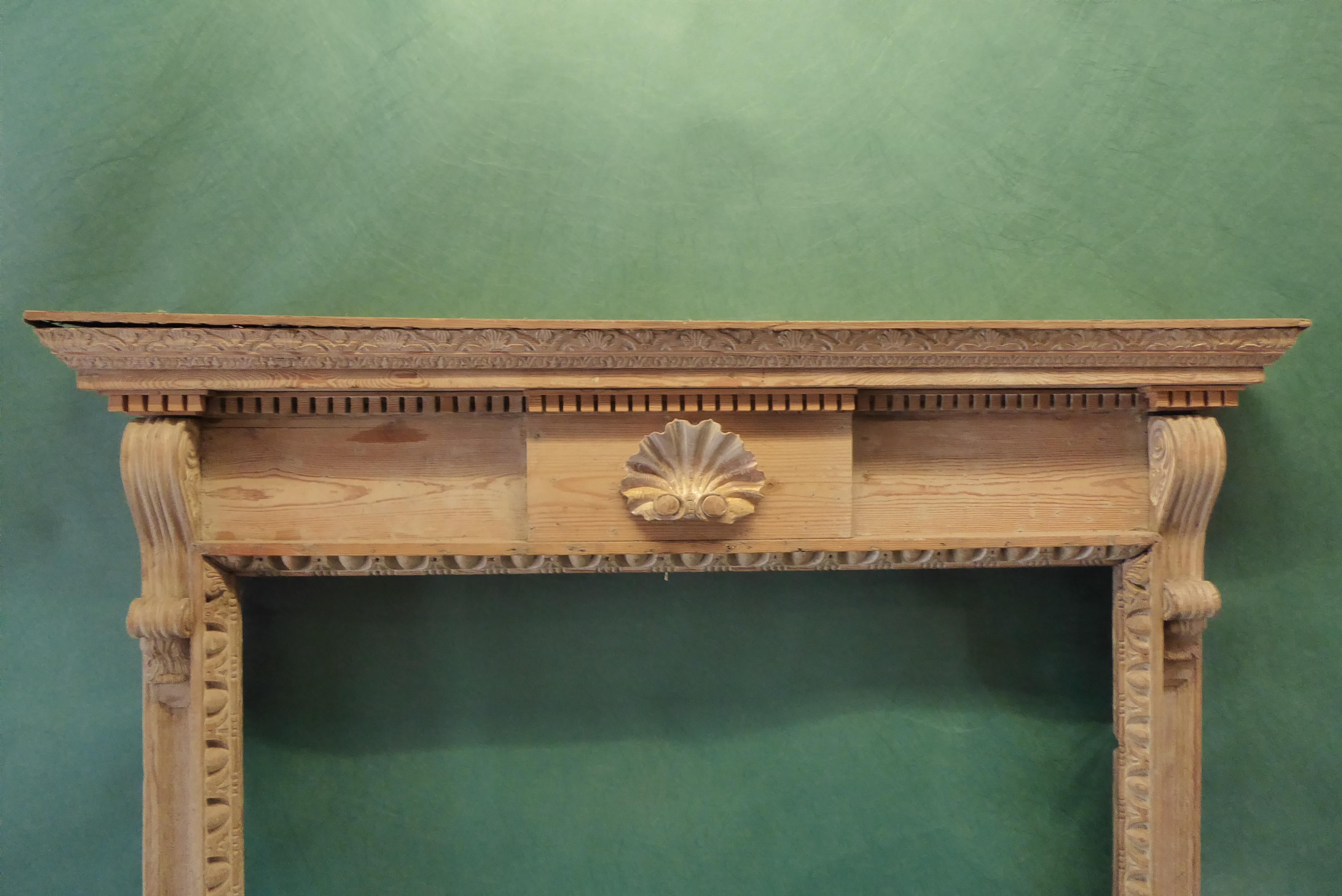 Cette cheminée ou manteau de cheminée en bois de pin sculpté de style George II. Le dessous de l'étagère est rehaussé de motifs floraux et d'étagères sculptés. La plaque de poitrine avec une coquille joliment sculptée. Les pieds sont ornés d'oves et