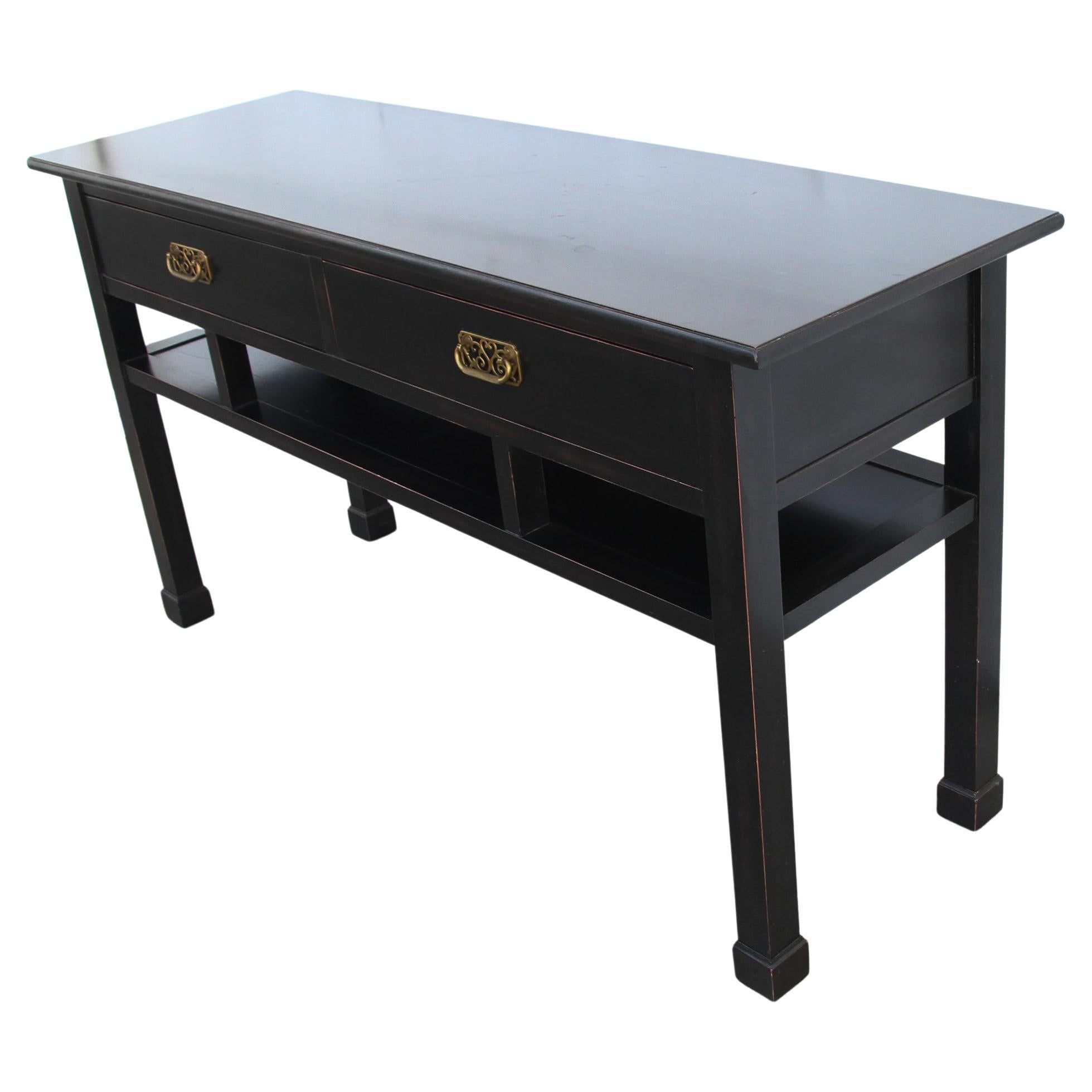 Chin Hua Baker style Ebonized console table

Ebonized chinoiserie console or sofa table in the style of Baker furniture. Featuring Ming style feet and two drawers with thin red reveals and beautiful brass pulls.
  