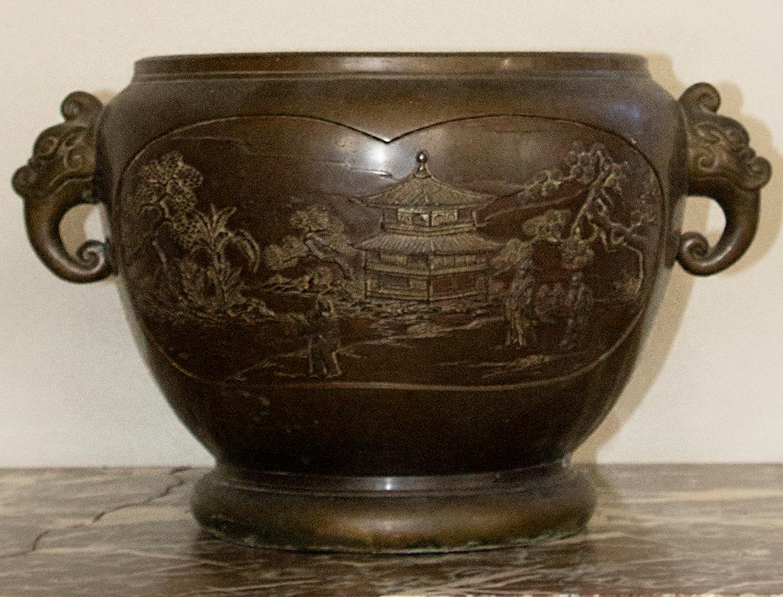Grand cache-pot en bonze avec une belle patine brune. Chaque côté du pot présente un décor représentant une scène de palais, les anses sont en forme d'éléphants stylisés.
Chine,
vers 1900.