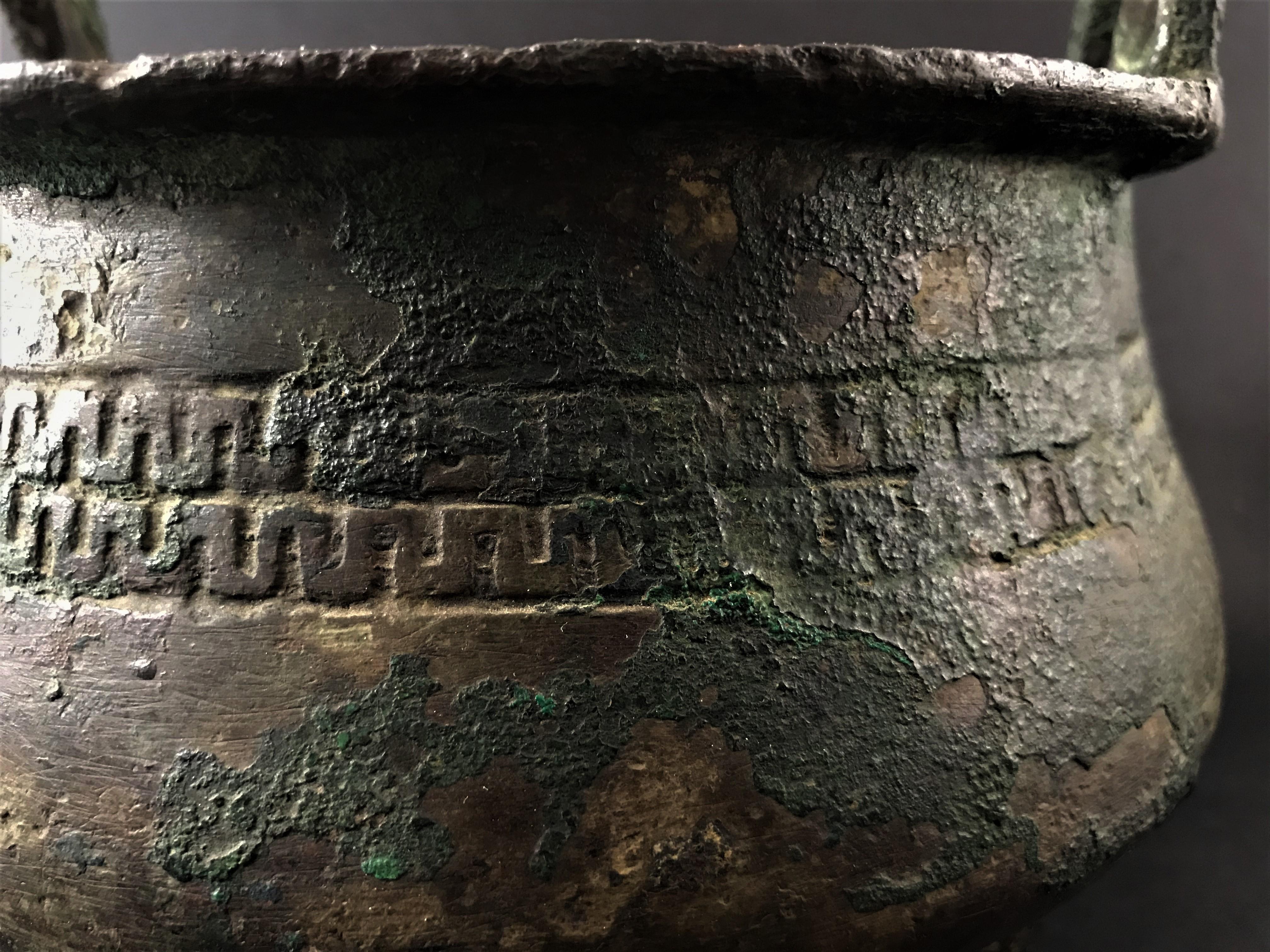 Bucket burns perfume in bronze resting on three feet. The body is sculpted with a band frieze with an archaic motif. Two inverted U-shaped handles punctuate the edge. This type of bronze bucket was cast with lost wax from molds in several parts and