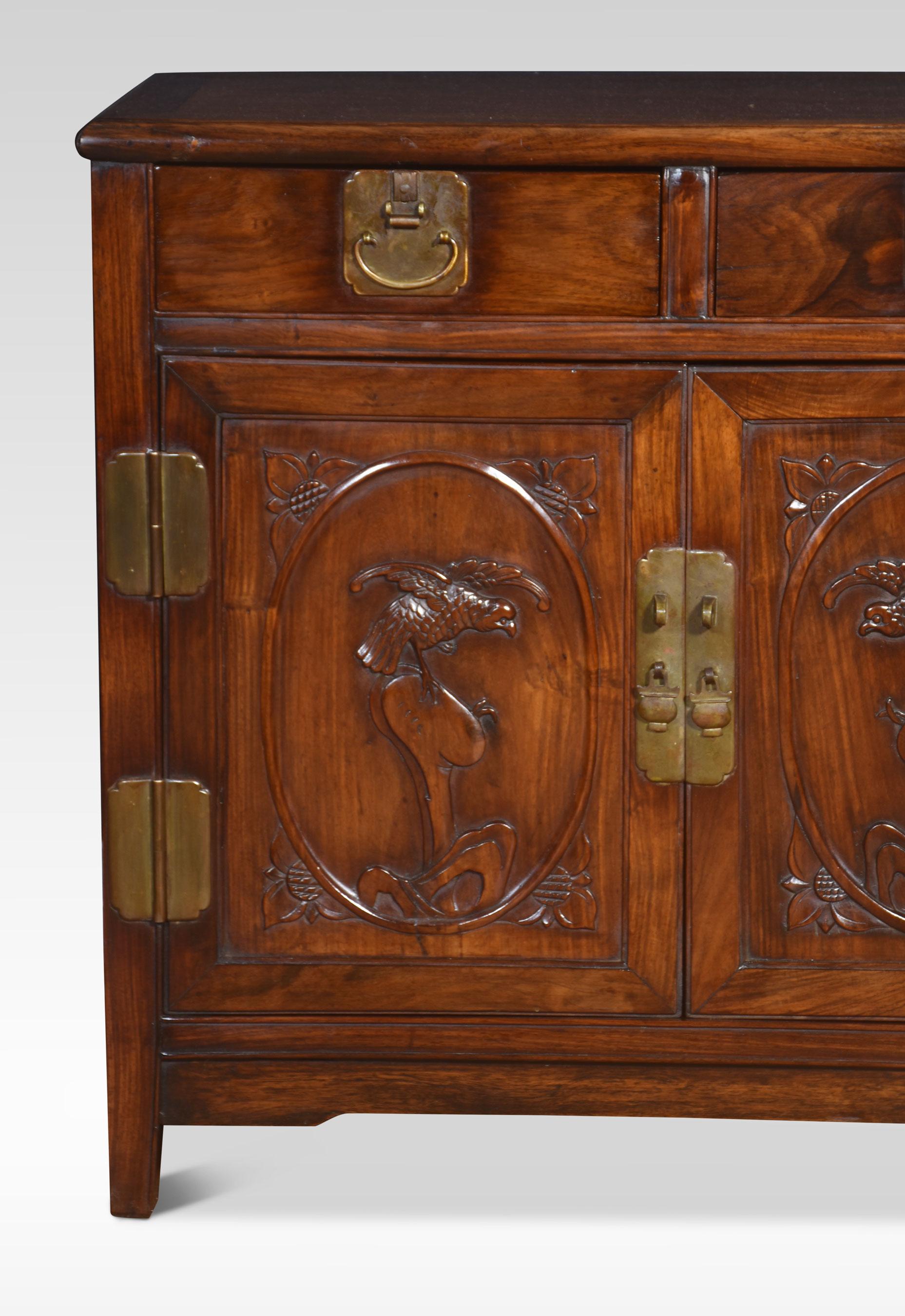 Chinese carved cupboard of small proportions, the rectangular figured top to the frieze fitted with two drawers with stylised handles. Above a pair of panelled cupboard doors with carved detail opening to reveal a single fixed shelf. All raised up
