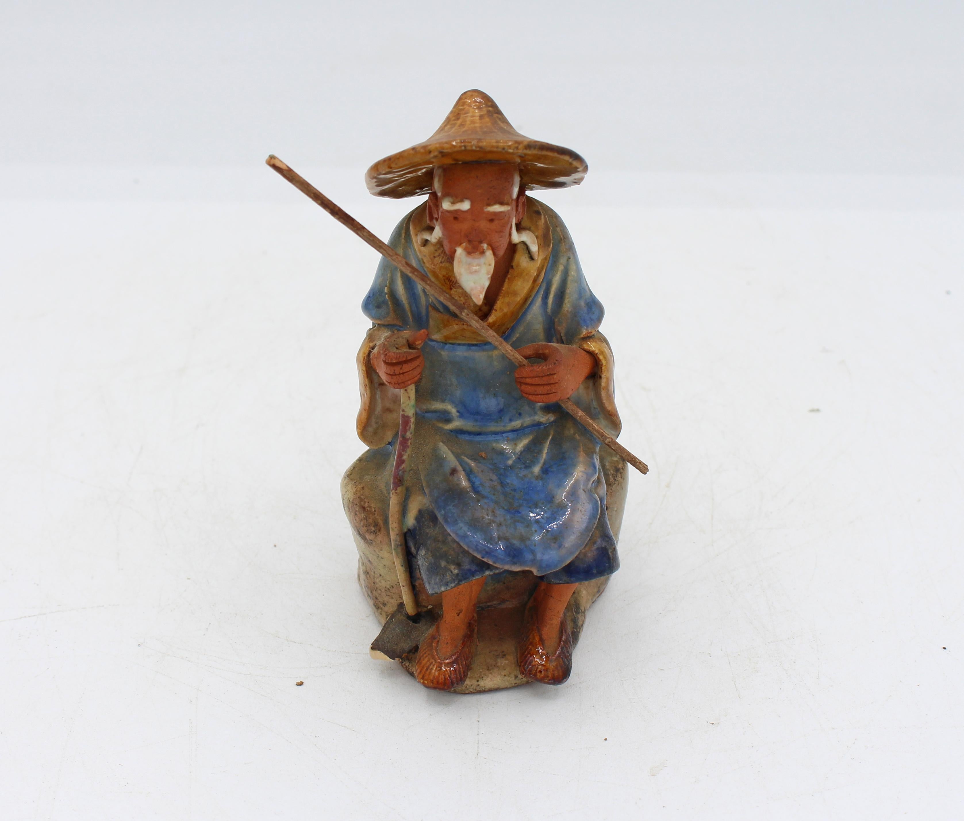 Souvenir dell'Esposizione Universale Cinese del 1891-1911 Figura di anziano contadino seduto, uomo di fango. Dimensioni moderate. Pelle abbronzata dal sole (ceramica non smaltata tinta con il tè). Cappotto blu foderato di giallo su pantaloni blu.