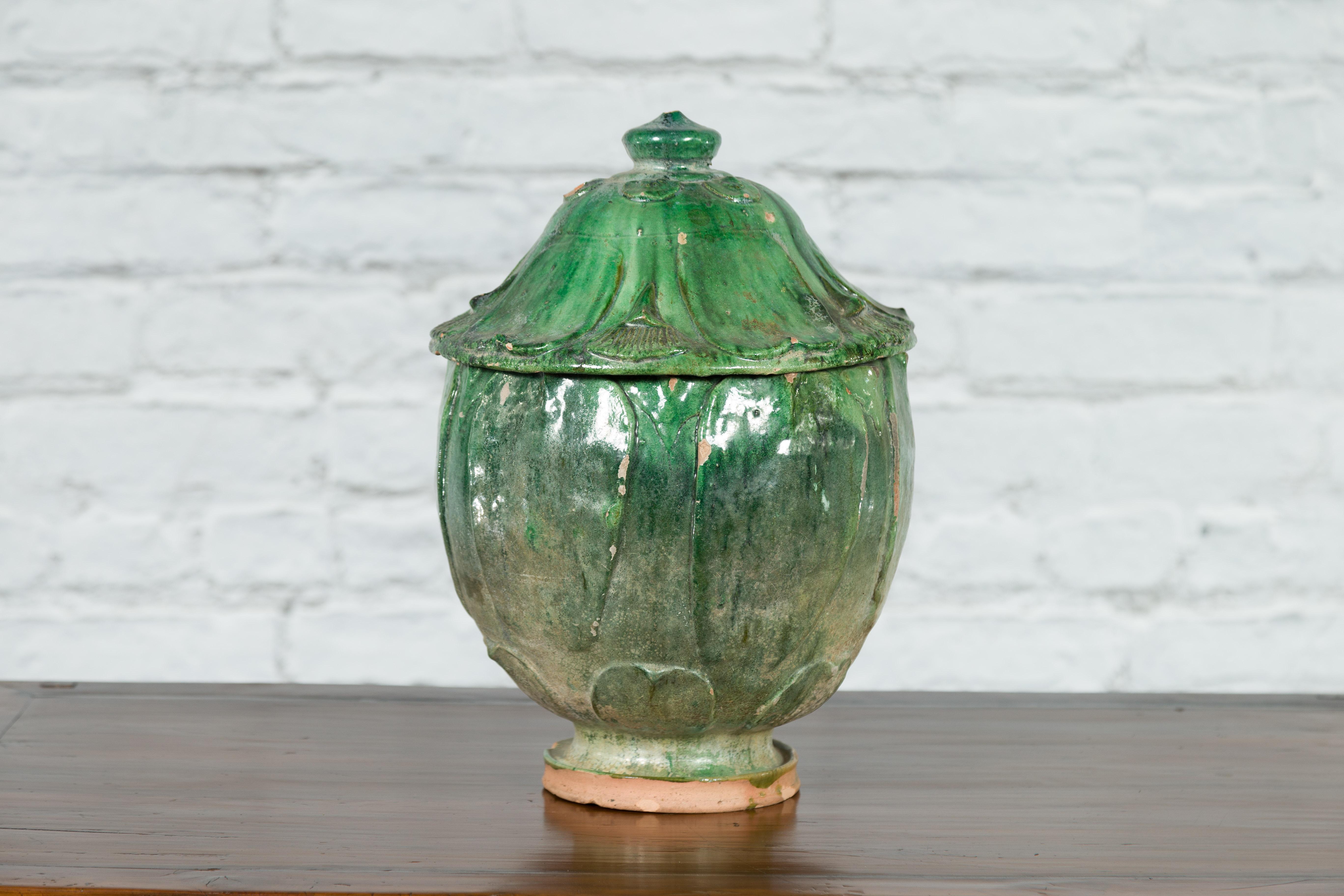 A Chinese Qing Dynasty period green glazed terracotta jar from the 18th century or earlier, with lotus design, lid and nicely distressed appearance. Created in China during the Qing Dynasty in the 18th century or at an even earlier time, this