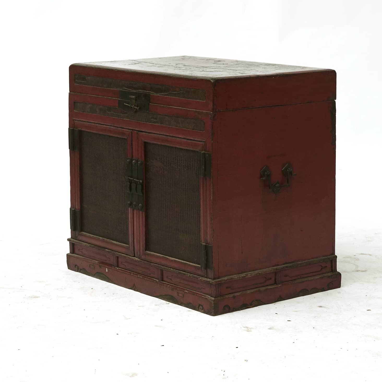 18th Century book chest in red lacquer.
The top lifts up to reveal an open interior storage compartment. Front with a pair of doors with fillings made of natural wicker. In between the doors is a bar, that can be removed making it possible to store
