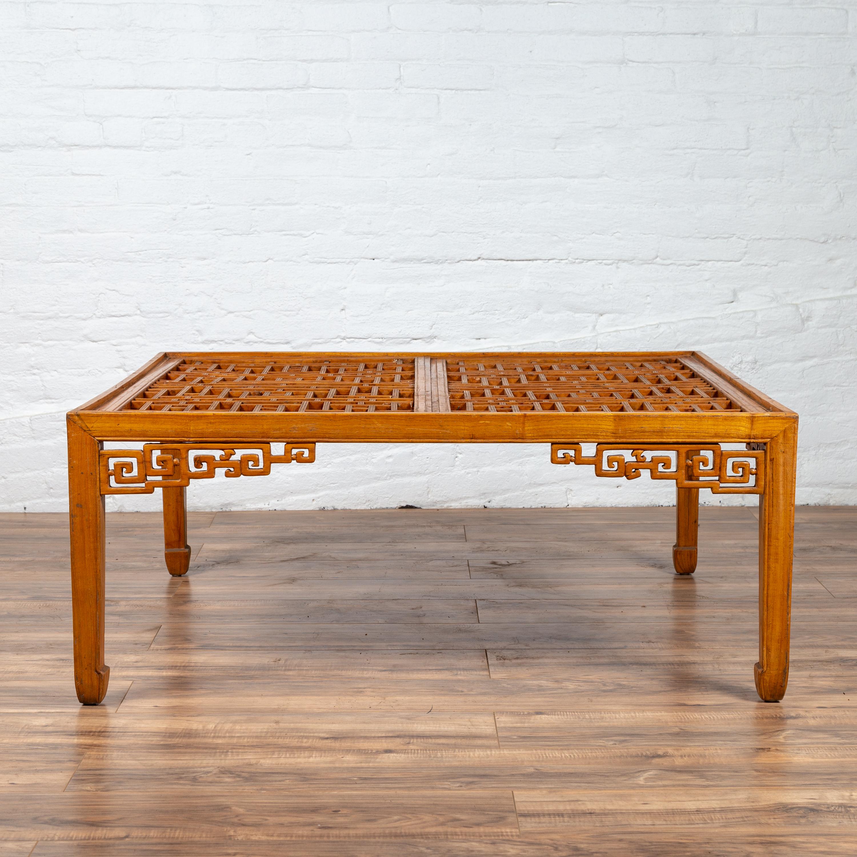 A Chinese elmwood square-shaped coffee table from the late 20th century, with open fretwork design and horse-hoof legs. Born in the later years of the 20th century, this Chinese coffee table features an exquisite rectangular top made of two panels