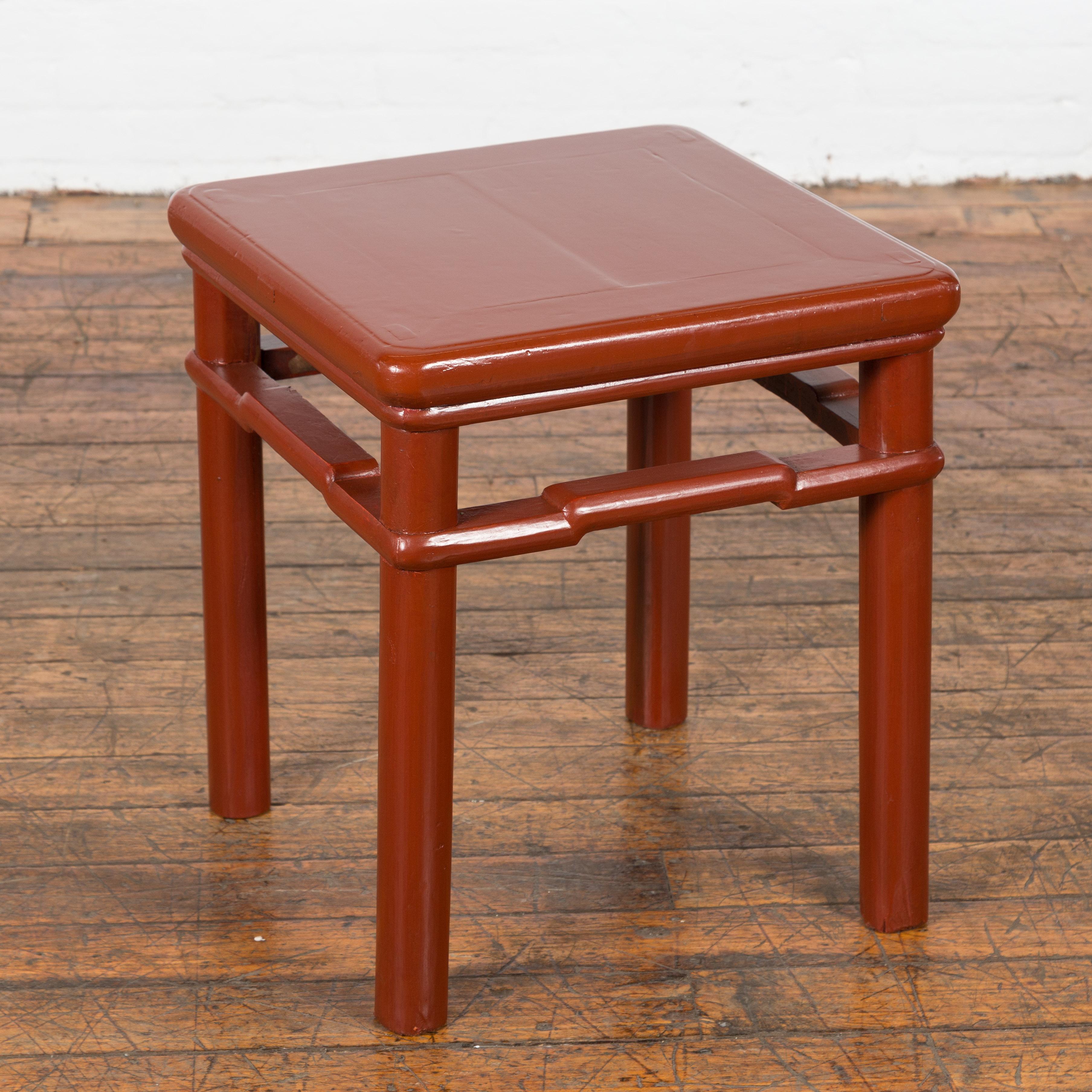 A Chinese late Qing Dynasty period side table or stool from the early 20th century, with red lacquer, humpback stretchers and straight cylindrical legs. This Chinese late Qing Dynasty period side table or stool from the early 20th century is a