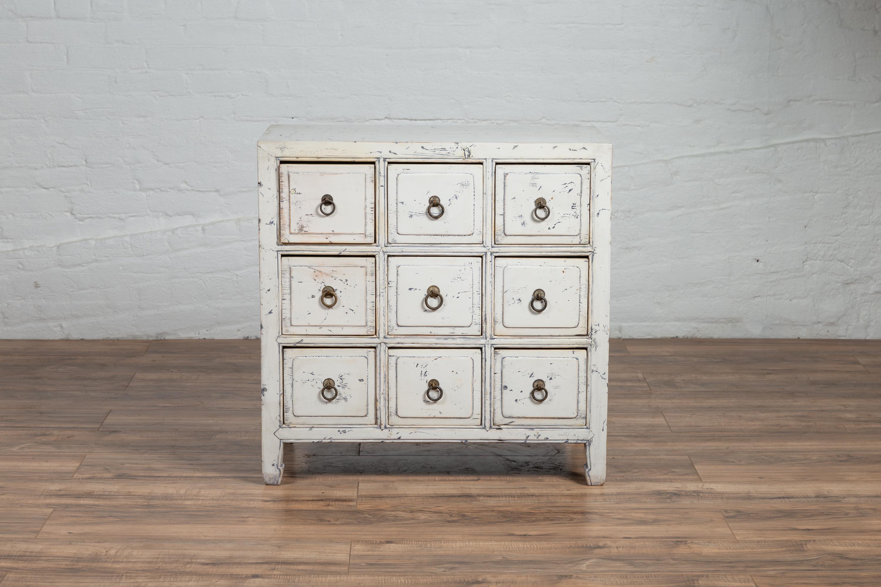 A vintage Chinese white painted nine-drawer apothecary chest from the mid-20th century, with distressed finish and black splatter. Born in China during the midcentury period, this charming apothecary chest features a rectangular top, sitting above a
