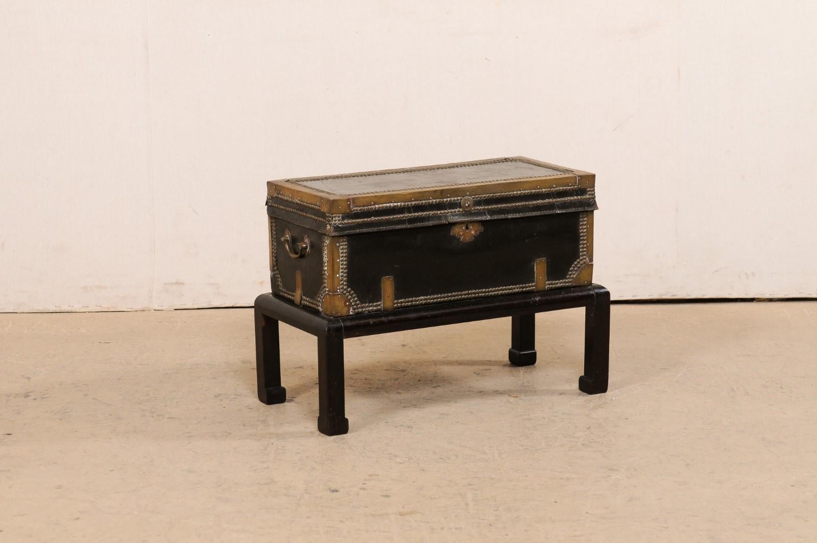A Chinese leather-wrapped wooden trunk with brass and nail-head accents from the 19th century, and raised on a vintage wood stand. This coffer from China has a rectangular-shape body, decorated with brass banding nicely outlining and defining the