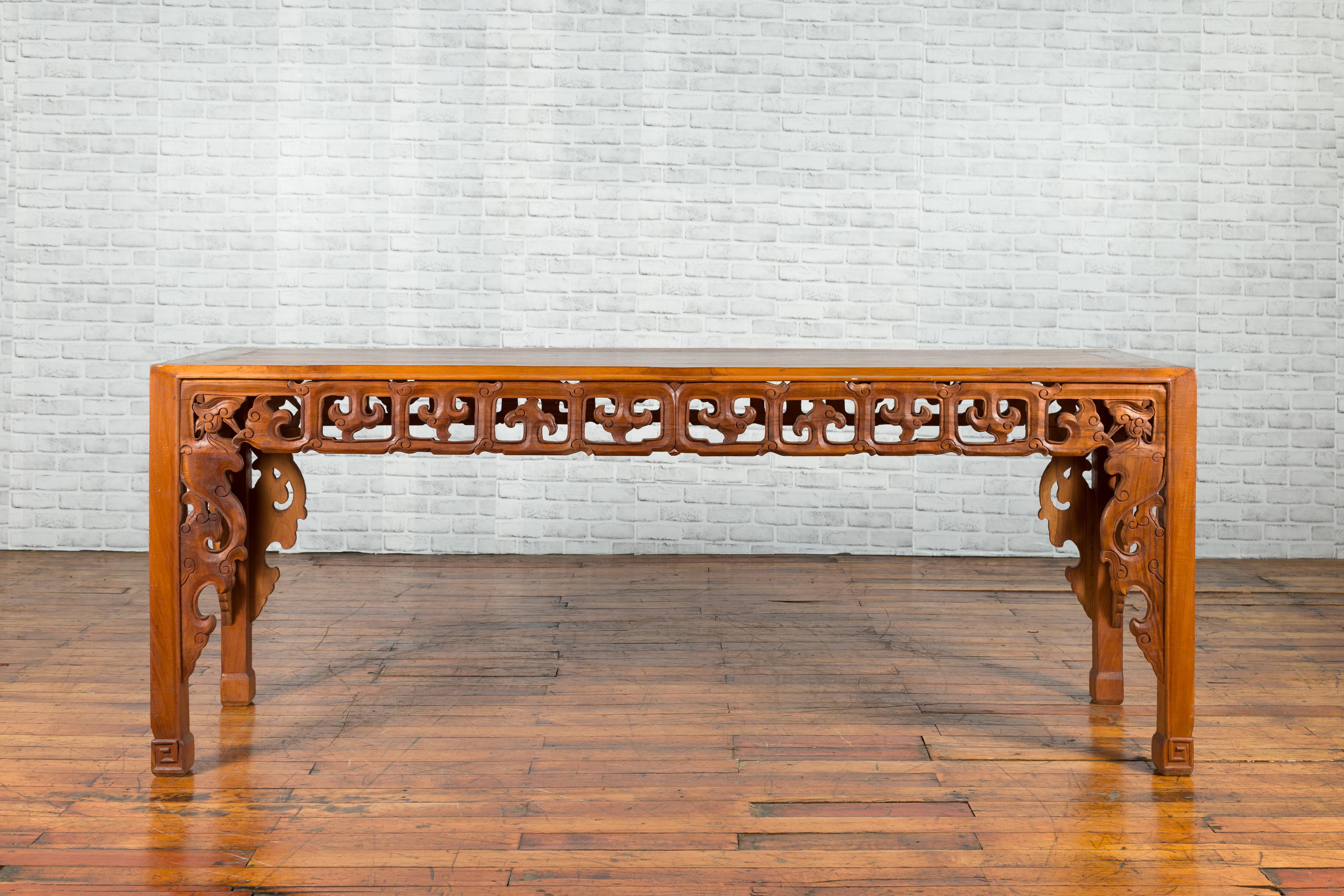 A Chinese Qing Dynasty period altar console table from the 19th century, with cloudy carved apron and scrolling feet. Created in China during the Qing Dynasty, this wooden console table features a rectangular top with central board, sitting above a