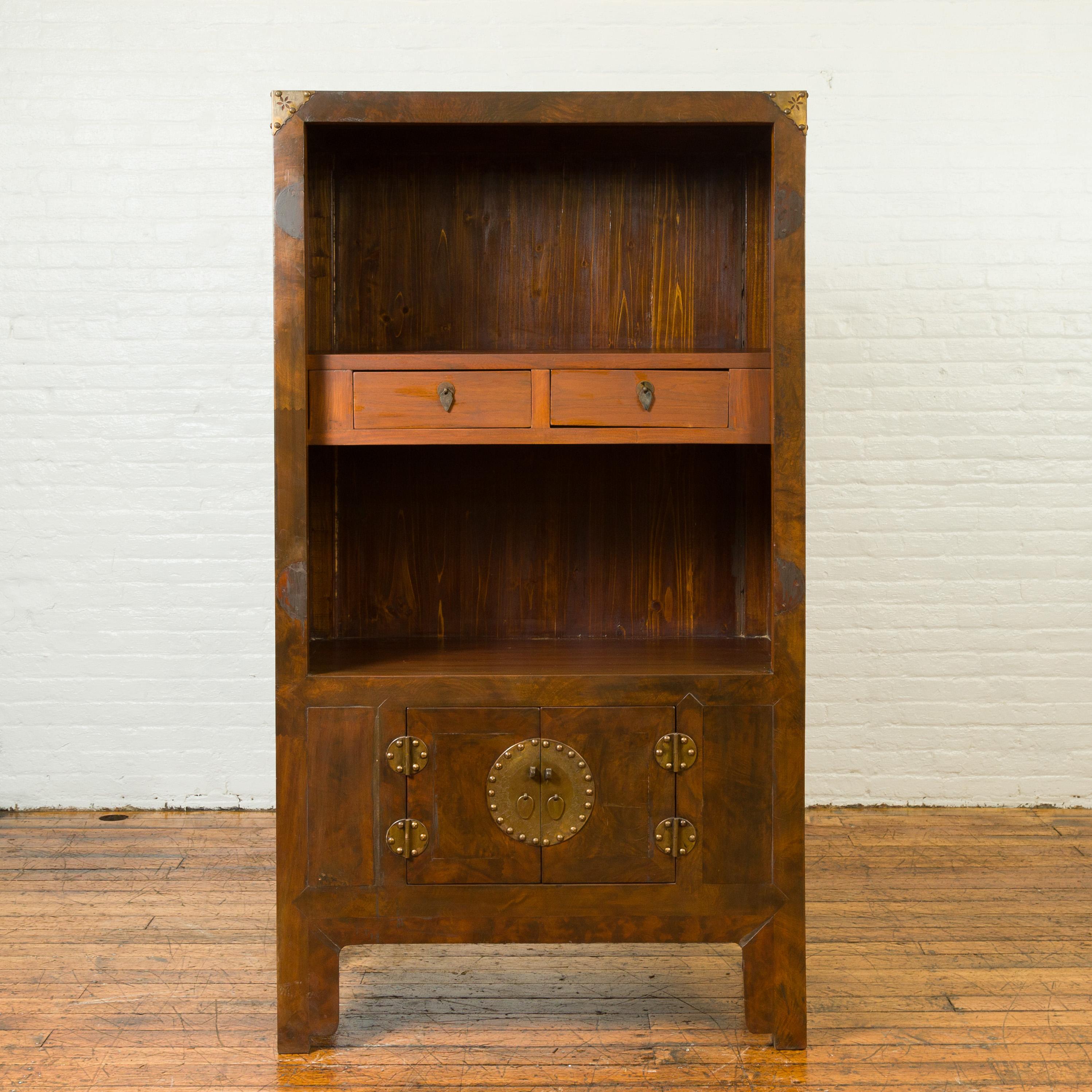 A Chinese antique elmwood bookcase cabinet from the 19th century, with two drawers, two doors and brass accents. Crafted in China from elm wood, this bookcase captures our eyes with its linear silhouette and subtly contrasting colors. The upper