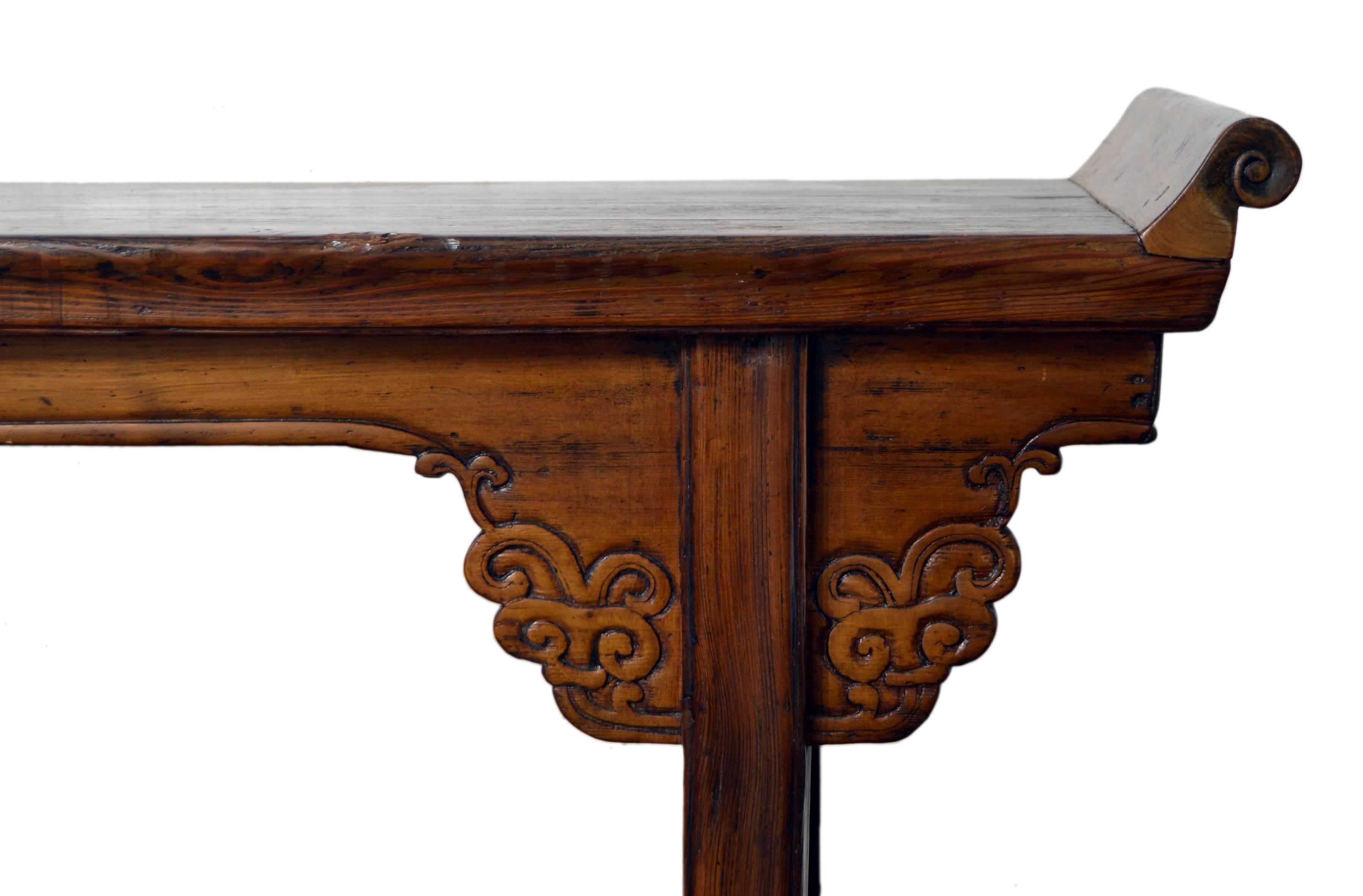 An antique Chinese wooden everted-flange altar console table from the 19th century with hand-carved scrolling motifs. This narrow Chinese altar table features a rectangular planked top, flanked with exquisite everted scrolling flanges. Our eye is