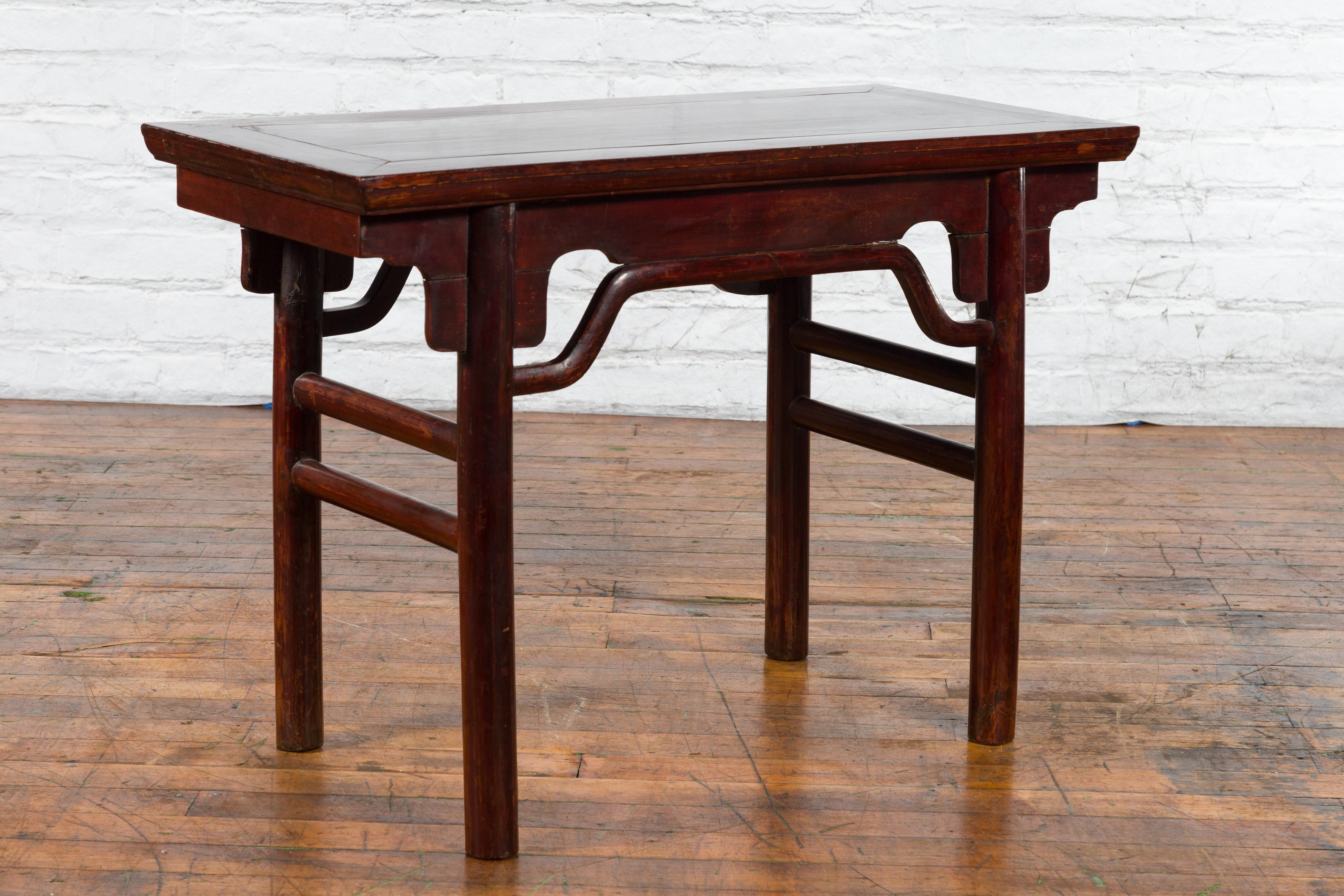 A Chinese Qing Dynasty period small altar console table from the 19th century with carved apron and side stretchers. Created in China during the Qing Dynasty, this small altar console table features a rectangular top with central board, sitting