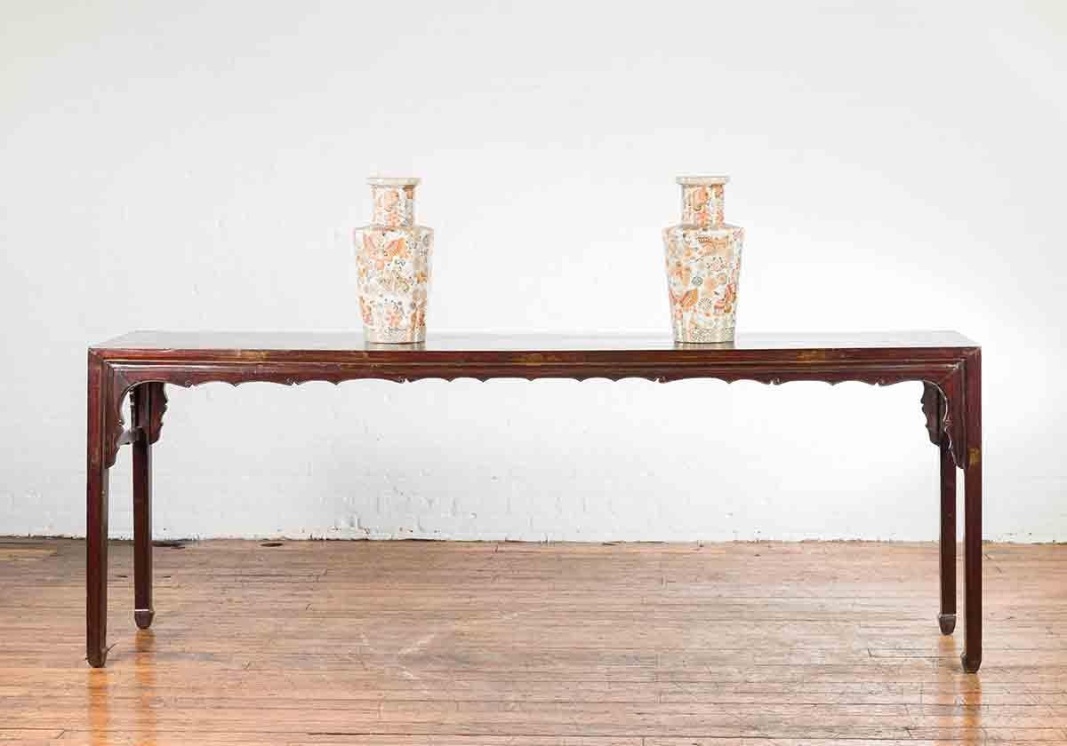 A Chinese Qing Dynasty period altar console table from the 19th century, with dark reddish brown patina. Created in China during the Qing Dynasty, this console table features a rectangular top with central board, sitting above a carved apron with