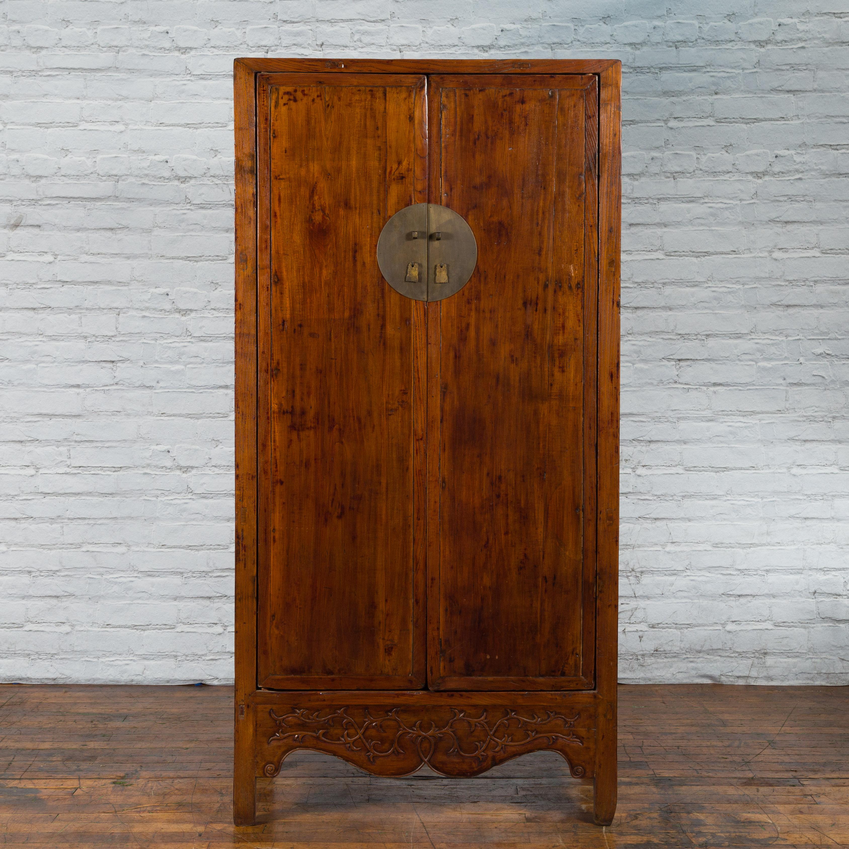 A Chinese Qing Dynasty period elm wood cabinet from the 19th century with two large doors, bronze medallion hardware, carved apron and inner shelves with hidden drawers. Created in China during the Qing Dynasty period in the 19th century, this large
