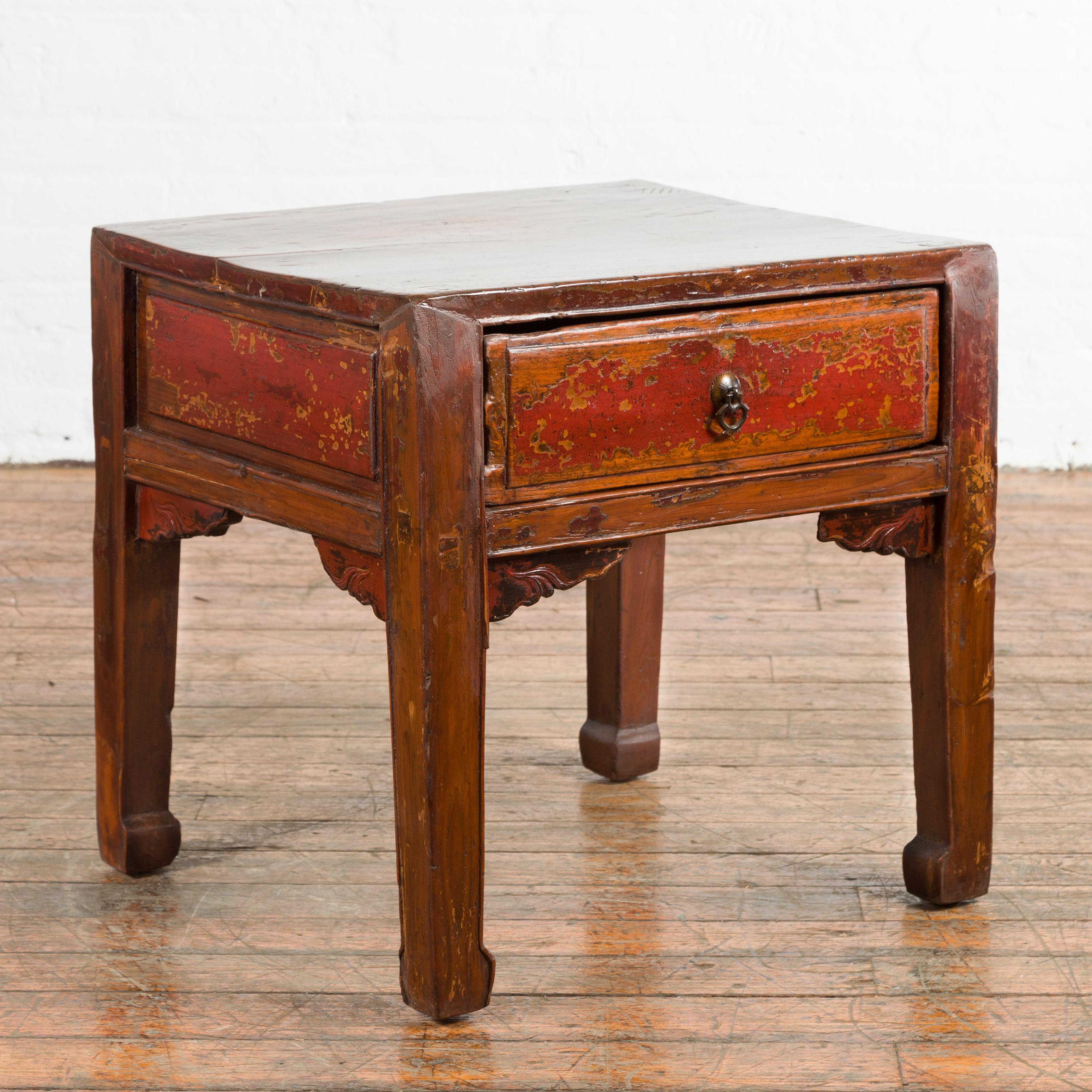 A Chinese Qing Dynasty period side table with single drawer from the 19th century, with horse hoof legs, cinnabar underglaze and distressed patina. Created in China during the Qing Dynasty, this side table features a rectangular top sitting above an