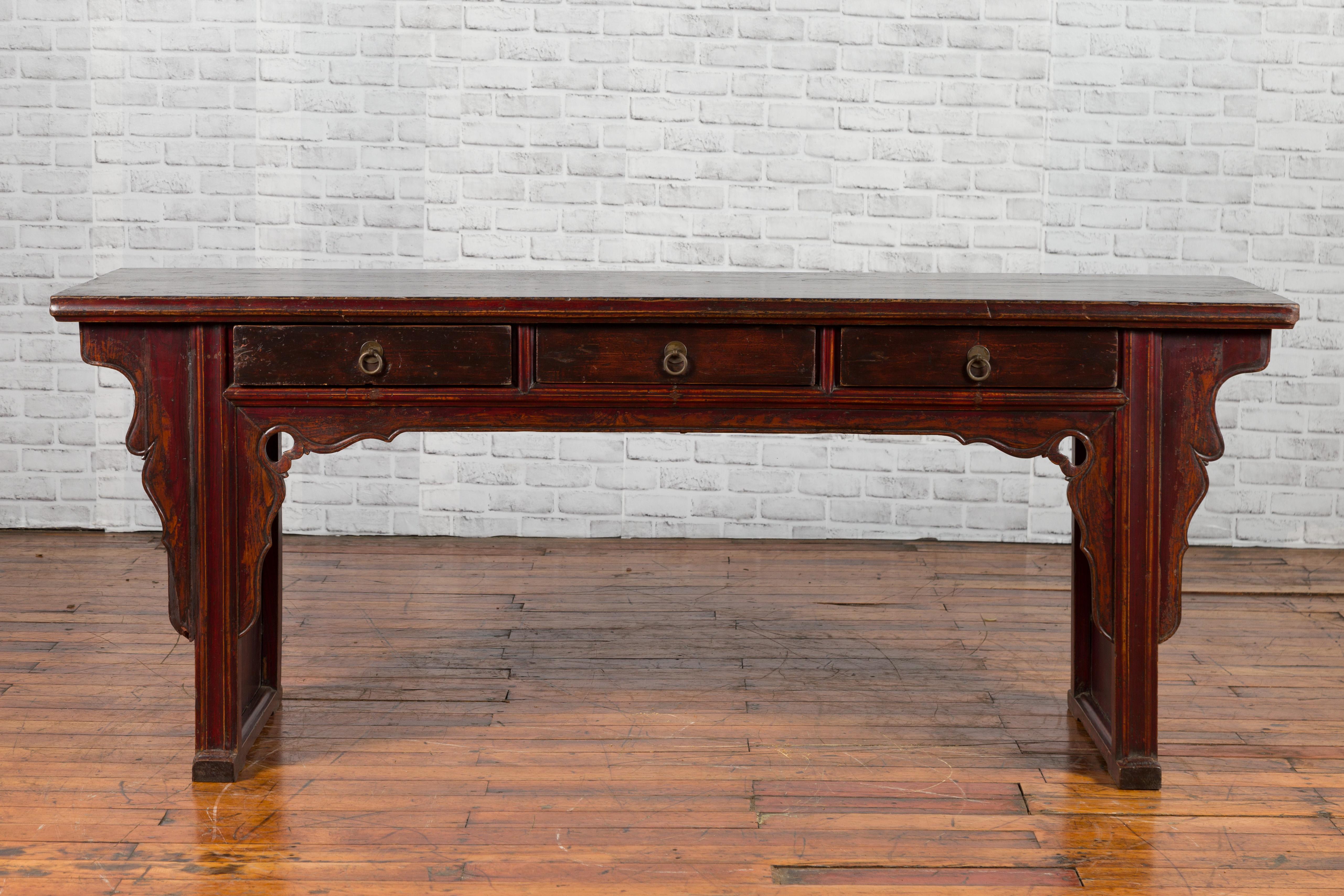 A Chinese Qing Dynasty period elmwood low console table from the 19th century, with three drawers and carved spandrels. Created in China during the Qing Dynasty, this elm console table features a rectangular top sitting above three drawers fitted