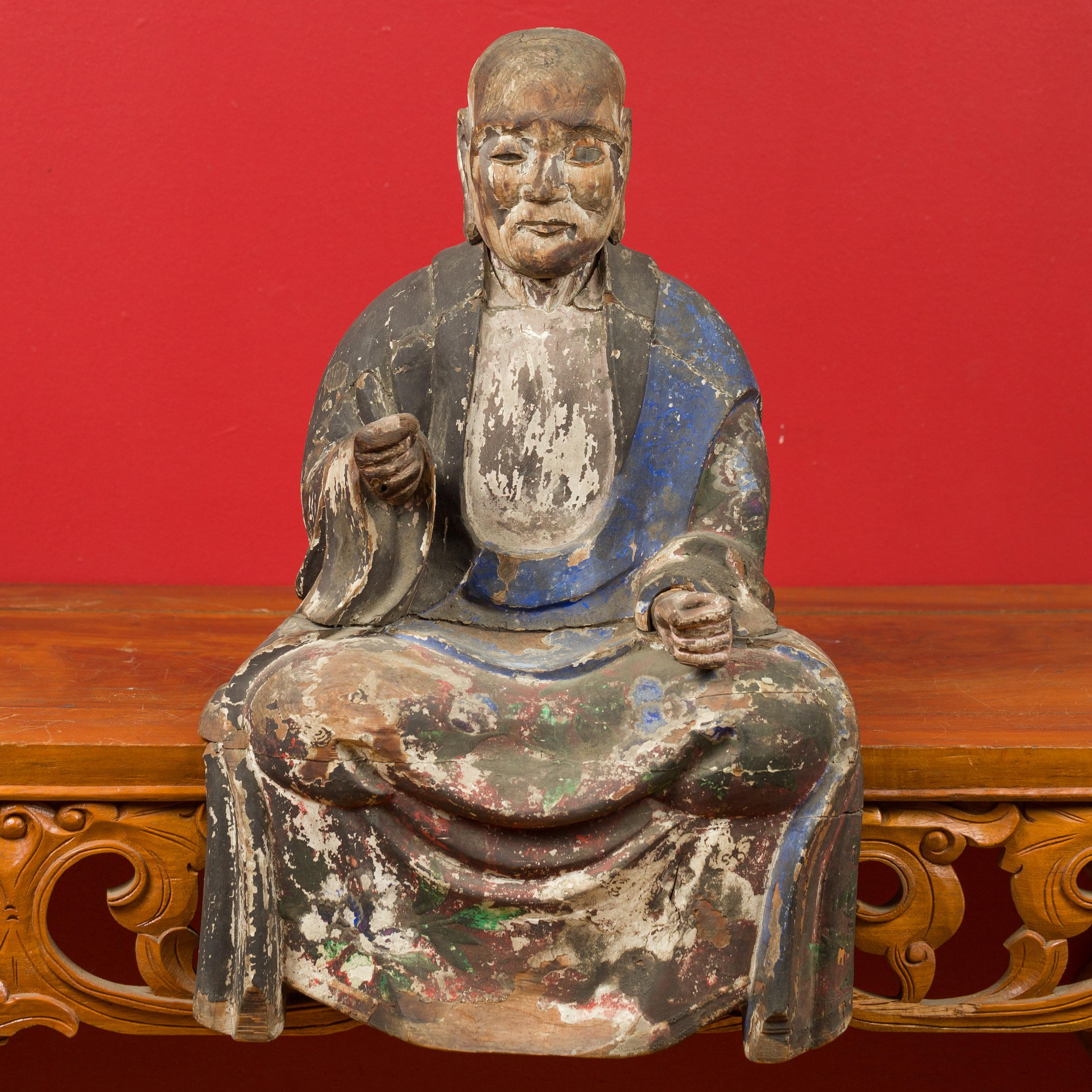 A Chinese Qing Dynasty period hand carved wooden seated Buddhist monk from the 19th century, with hand painted details and glass eyes. Born in China during the Qing Dynasty (1644-1912), this statue features a seated monk presenting traces of its