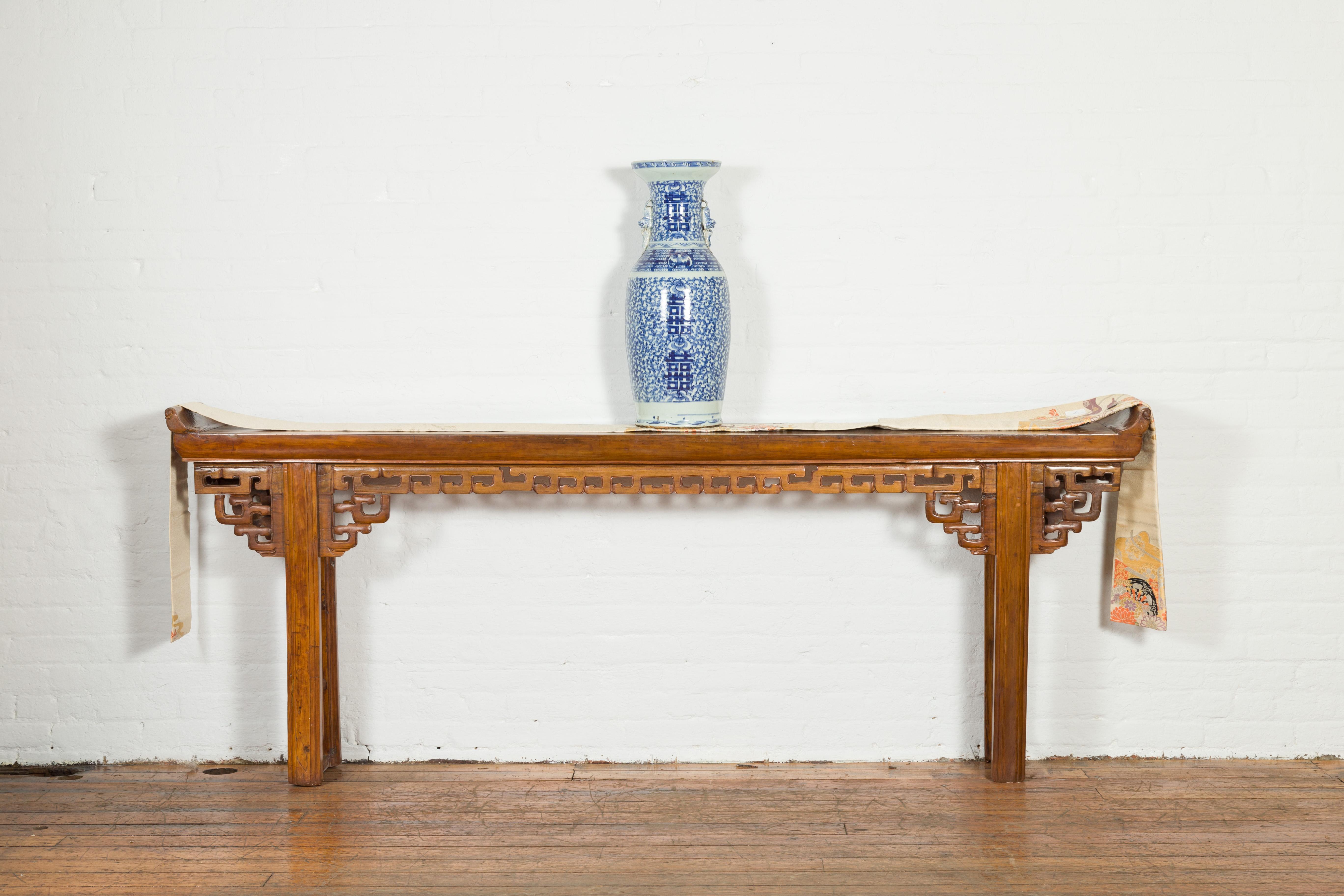 A Chinese Qing dynasty period altar console table from the 19th century, with everted flanges and open fretwork. Created in China during the 19th century, this Qing dynasty altar table features a narrow rectangular top with everted flanges, sitting