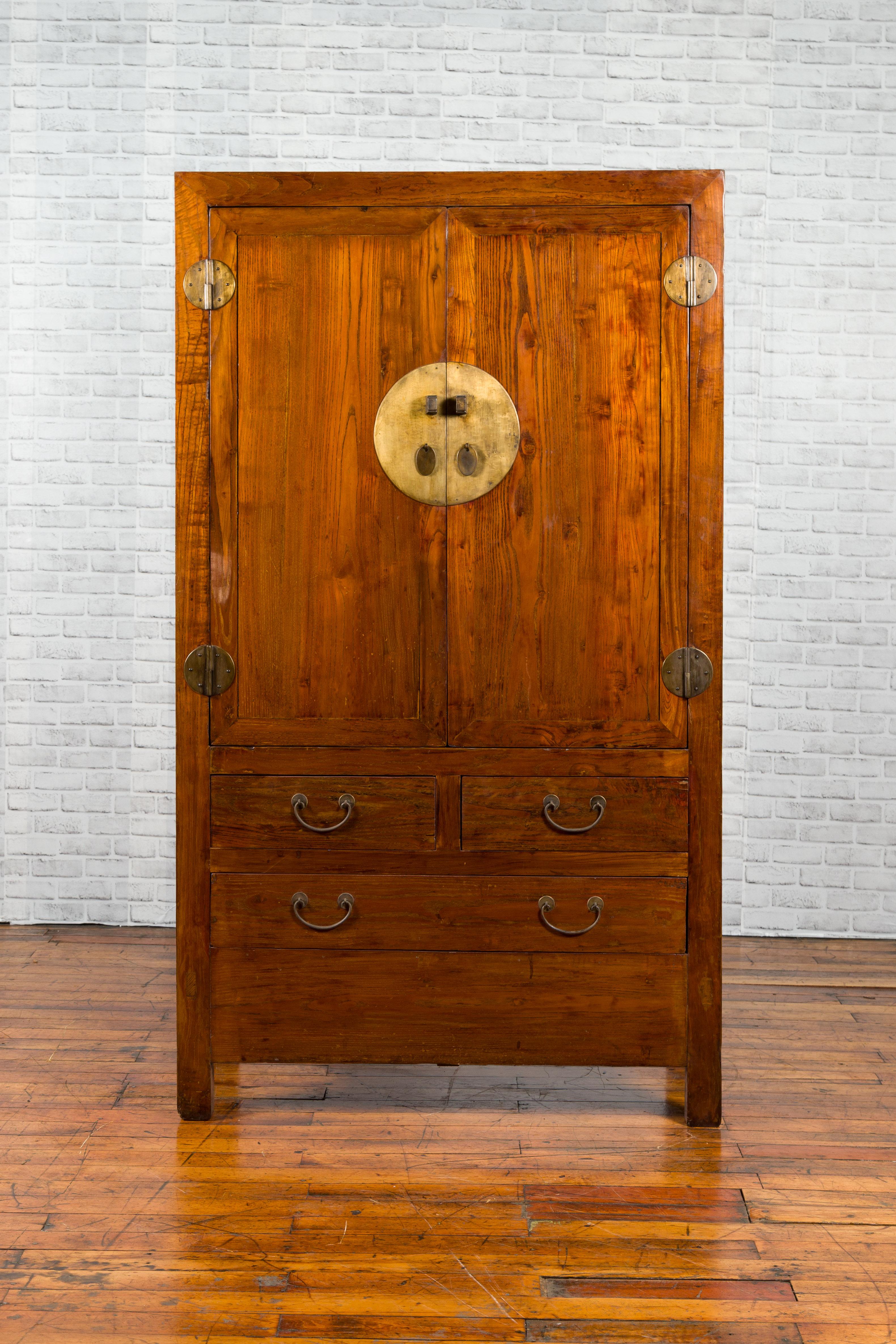 A Chinese Qing Dynasty period elm cabinet from the 19th century, with two doors, three drawers and brass hardware. Created in China during the Qing Dynasty, this cabinet features a linear silhouette perfectly complimenting the warmth of the elm