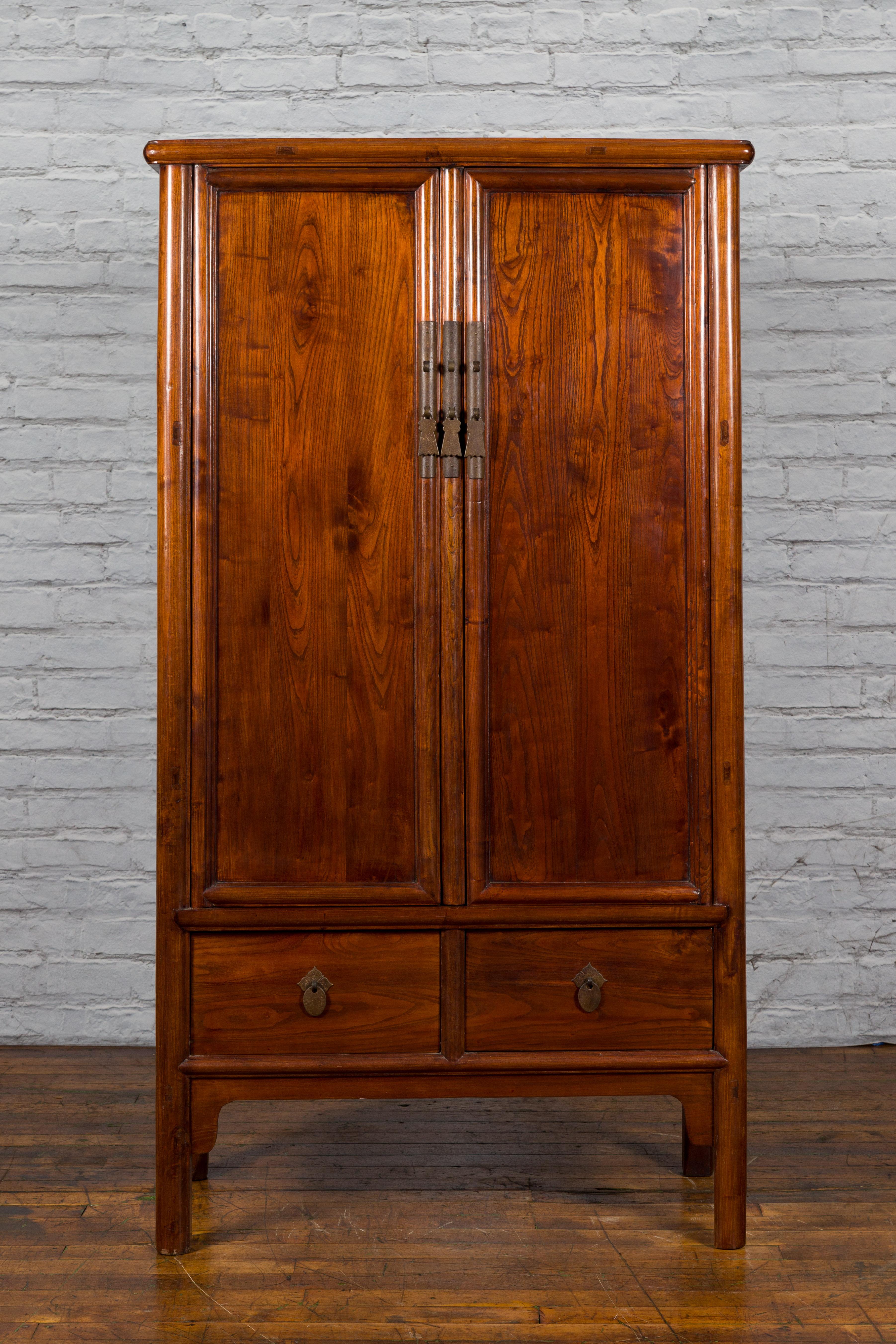 A Chinese Qing Dynasty period elmwood cabinet from the 19th century with tapered silhouette and two drawers. Created in China during the Qing Dynasty era, this elmwood noodle cabinet features a tapering silhouette perfectly complimented by a warm