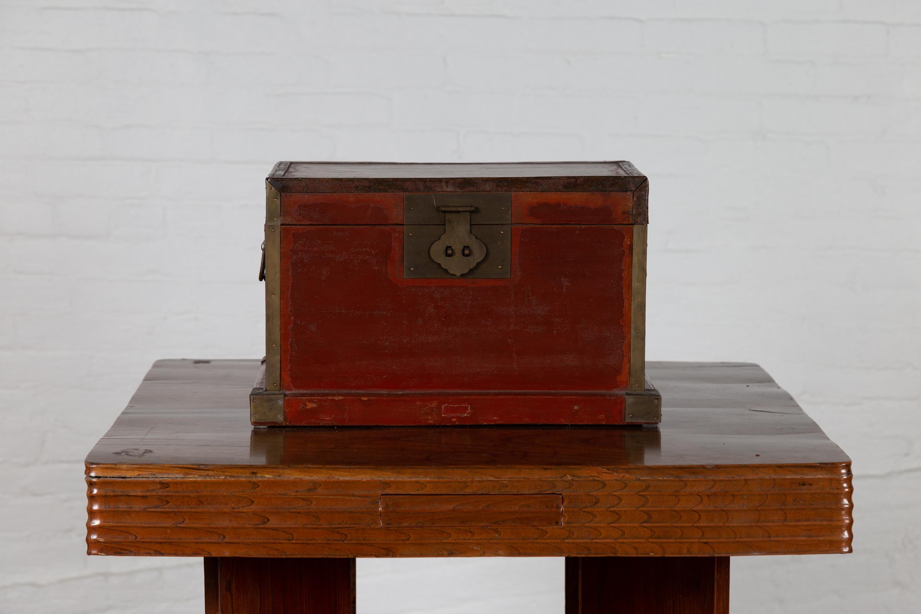 A Chinese red lacquered treasure chest box from the 19th century, with brass hardware. Born in China during the 19th century, this elegant treasure chest features a red lacquered surface (with deeper red standing out on a lighter color), beautifully