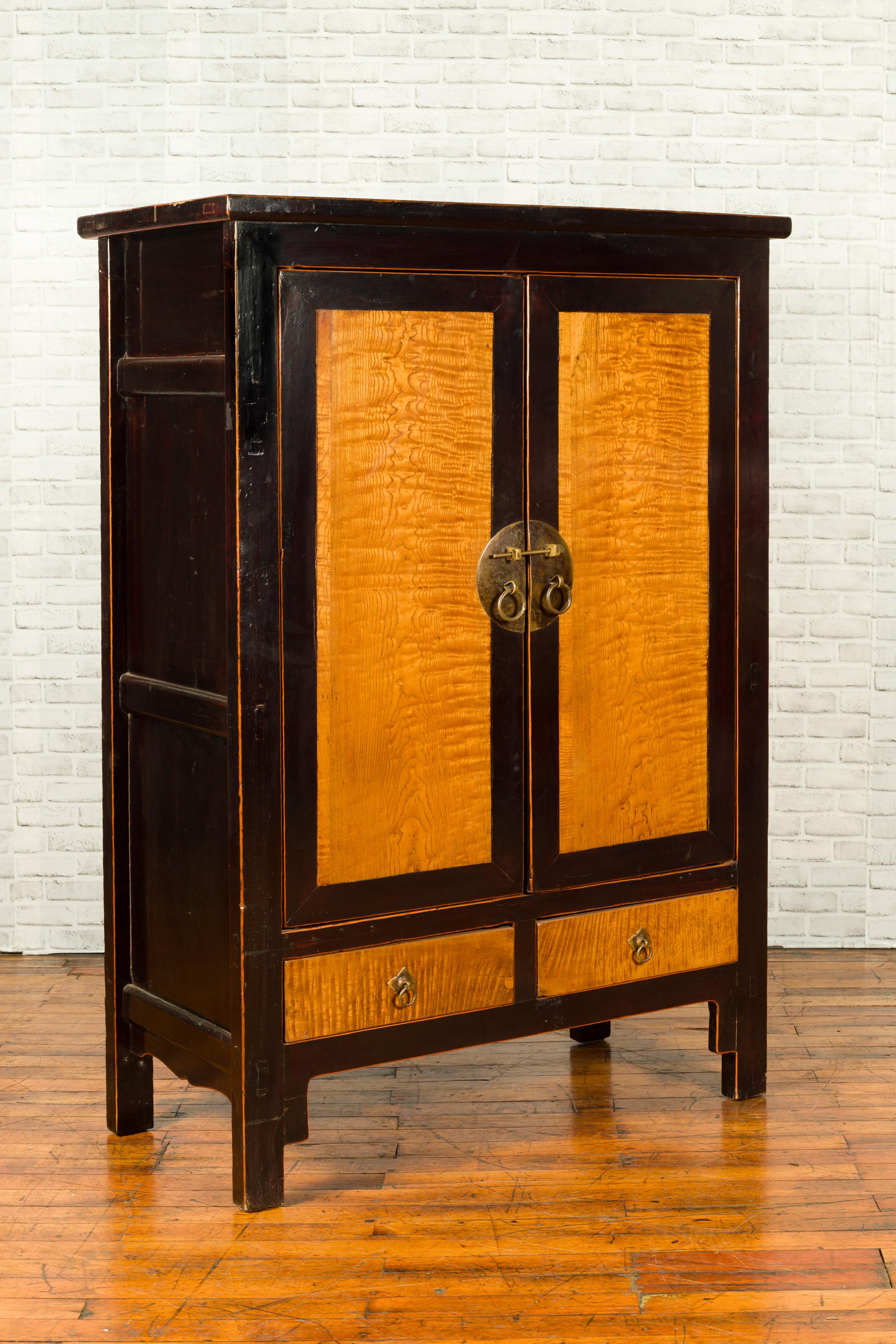 A Chinese black cabinet from the 19th century, with inset burl wood panels, drawers and brass medallion. Created in China during the 19th century, this cabinet captures our attention with its contrasting colors and linear silhouette. Two doors,
