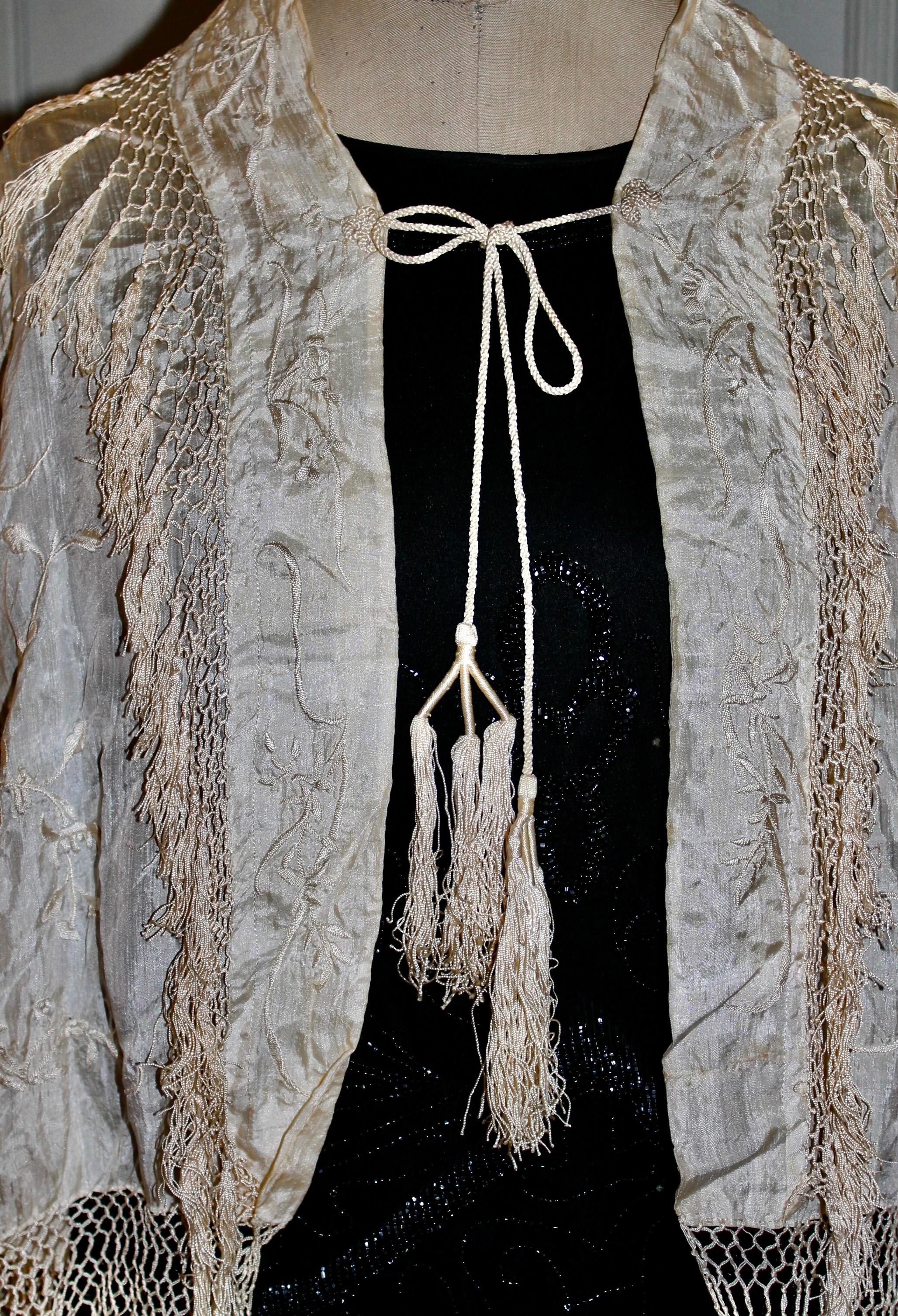 Cream silk.  Hand embroidered with a floral motif.  Hand knotted silk fringe.  Hanging braided tassels on back.  Tassels add 5