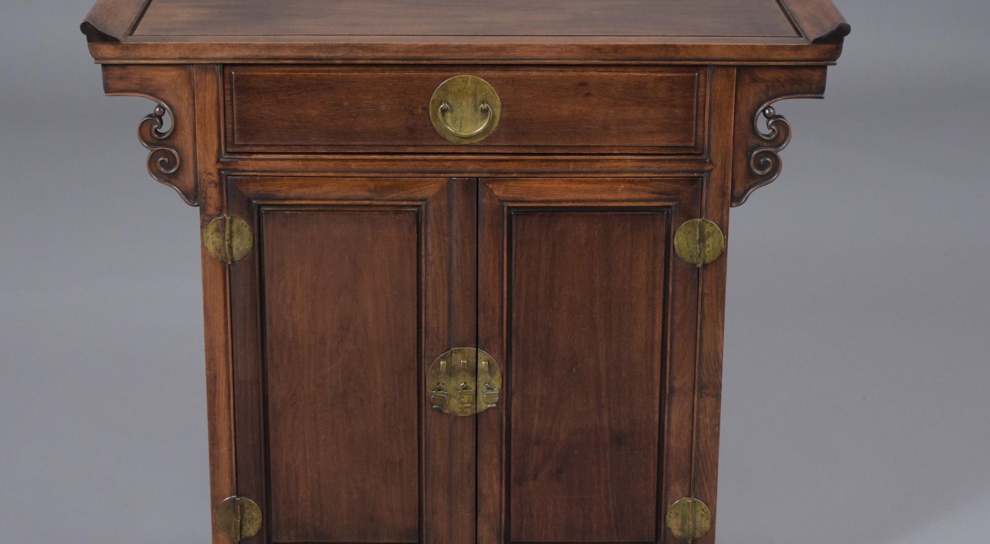 A vintage Chinese console made out of mahogany wood features a dark mahogany color and carved arched motifs. This fabulous piece comes with a single drawer, double doors with brass handles and the interior has a single shelf. This 1950's carved