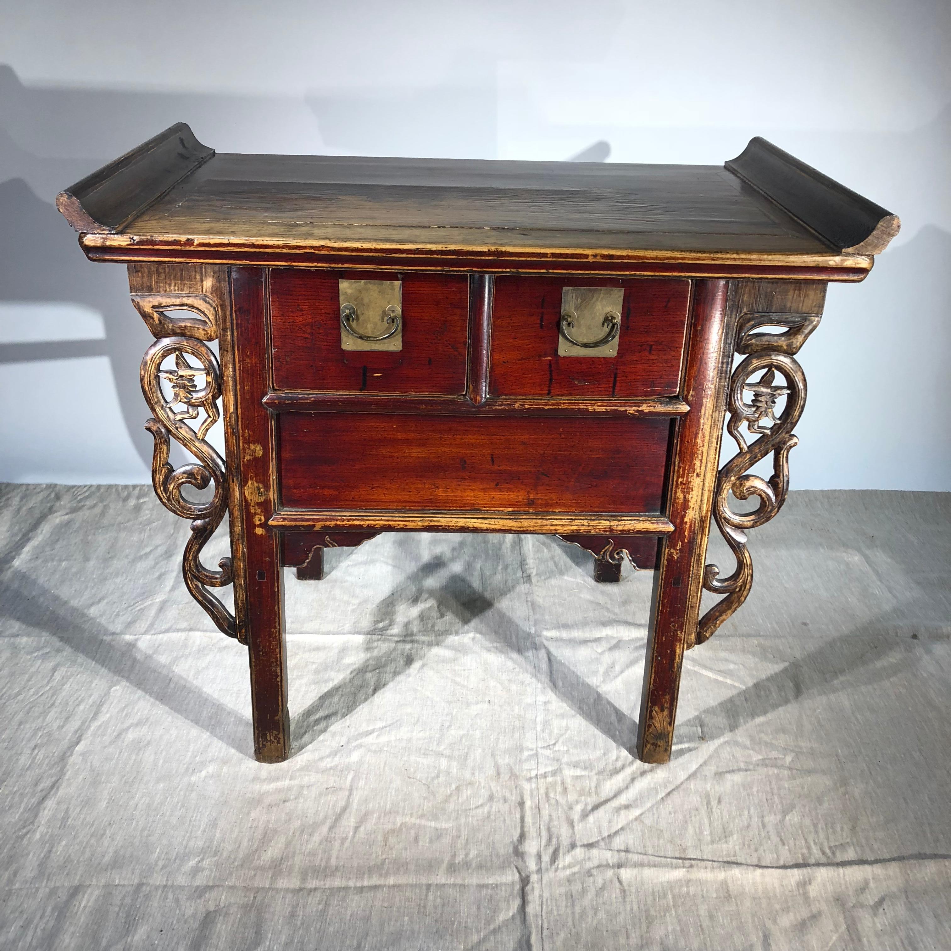 A Chinese altar table in stained and lacquered elm with carved side decoration and two drawers with original hardware. 
 