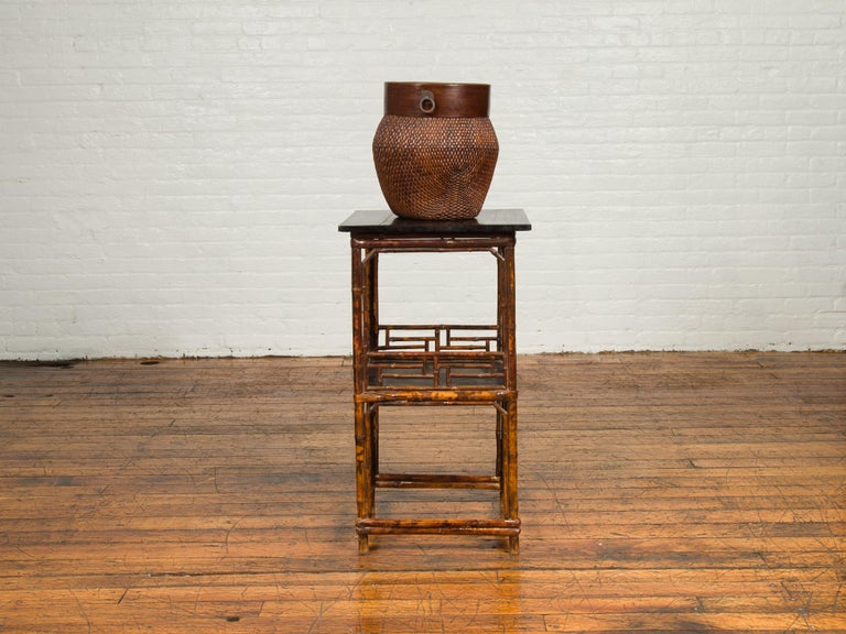 A Chinese antique bamboo lamp table from the early 20th century, with shelf and black top. Born in China during the early years of the 20th century, this lamp table features a square black top sitting above a bamboo base with geometric patterns and