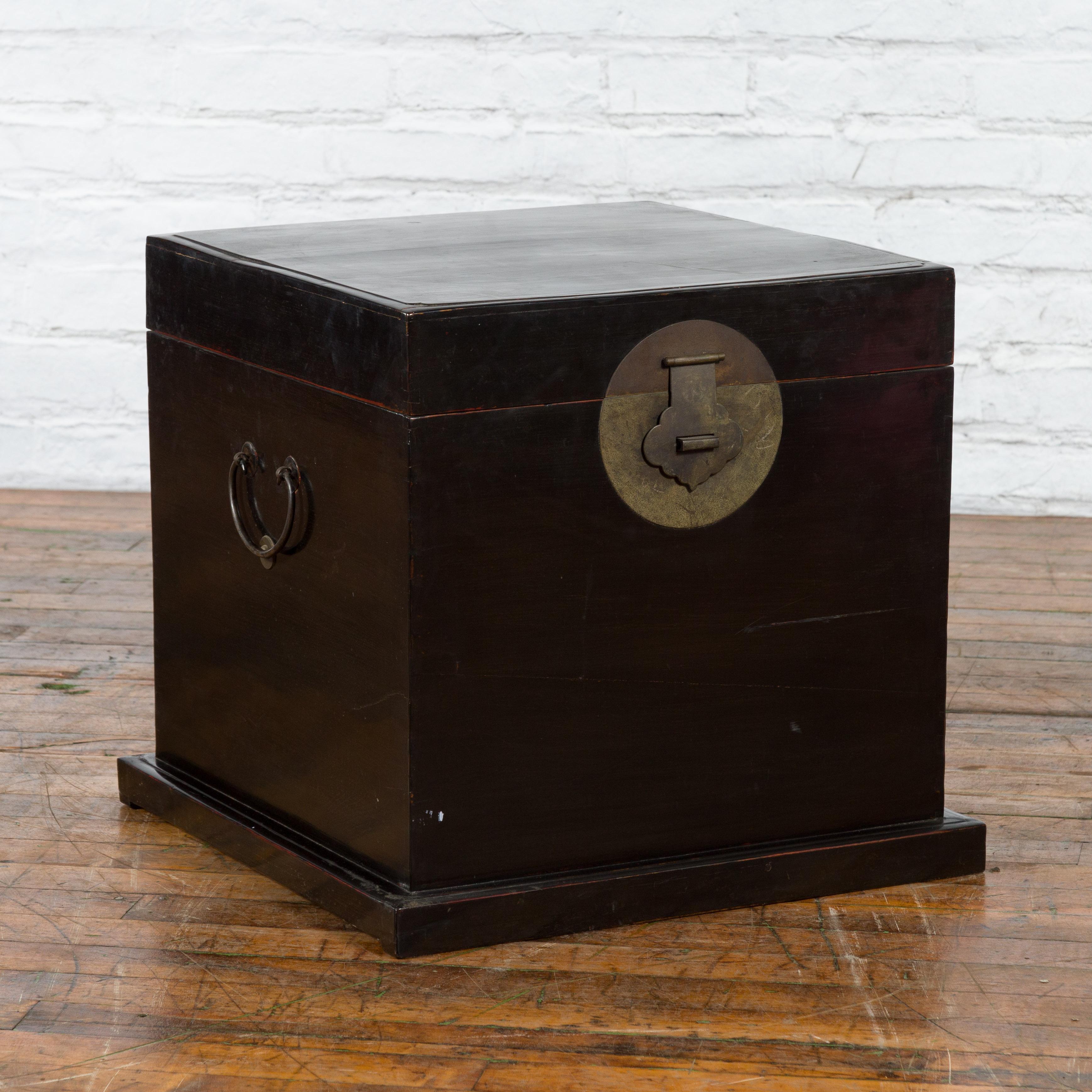 A Chinese black lacquer trunk from the early 20th century with large brass medallion and lateral C-scroll handles. Created in China during the early years of the 20th century, this trunk features a black lacquer perfectly complimenting its