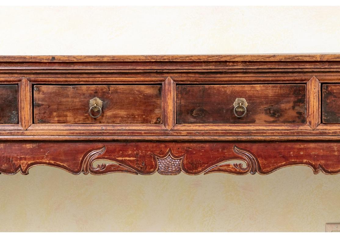 A notable late 19th century carved wood altar table in old red and black paint now worn to a nice patina with a particularly decorative form. The plank top with tenons and carved edge. The elaborate upper apron with carved openwork ends with scrolls