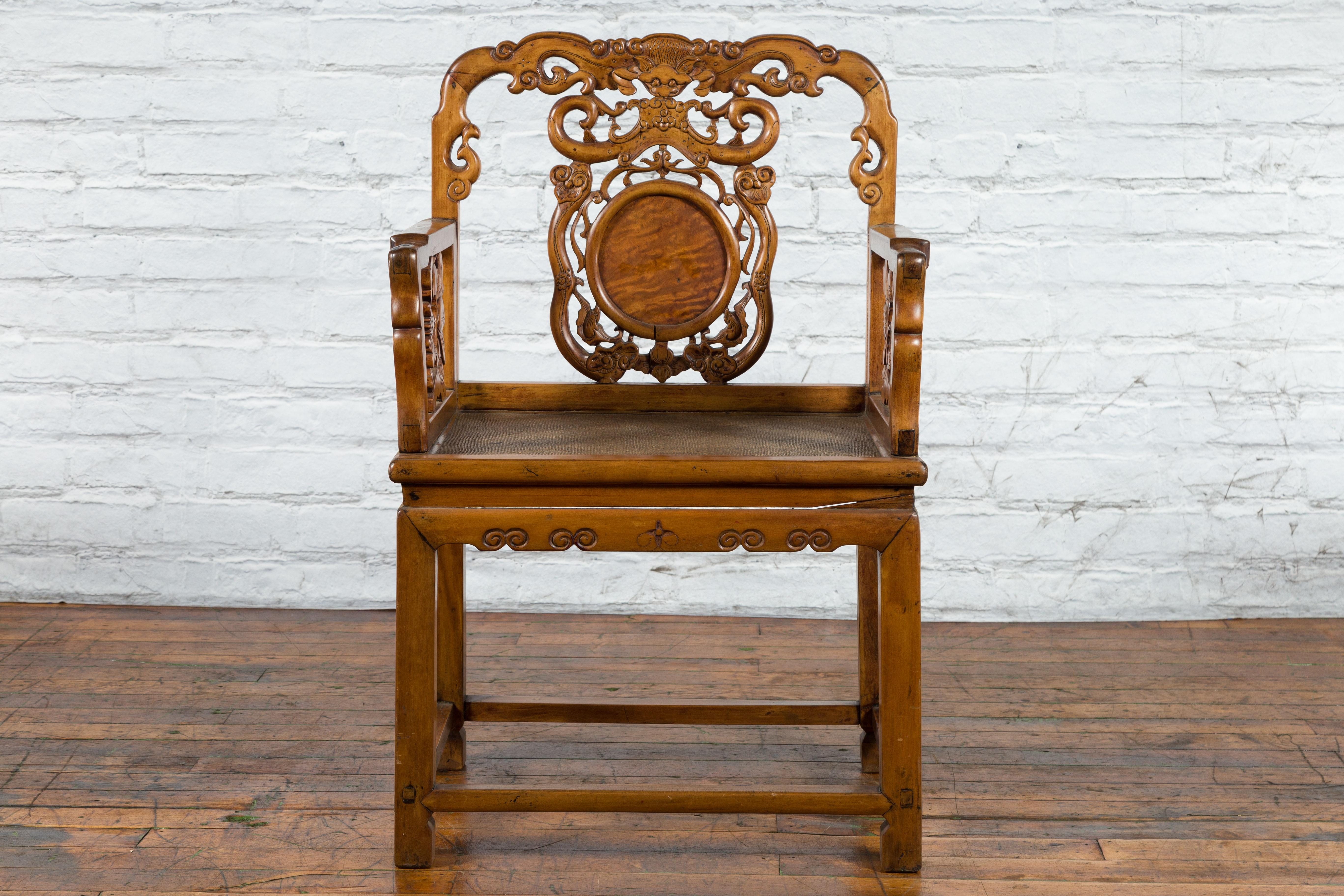 A Chinese antique wooden armchair from the early 20th century with hand-carved back and arms, and hand-woven rattan seat. Created in China during the early years of the 20th century, this unusual wooden chair features a mesmerizing back adorned with