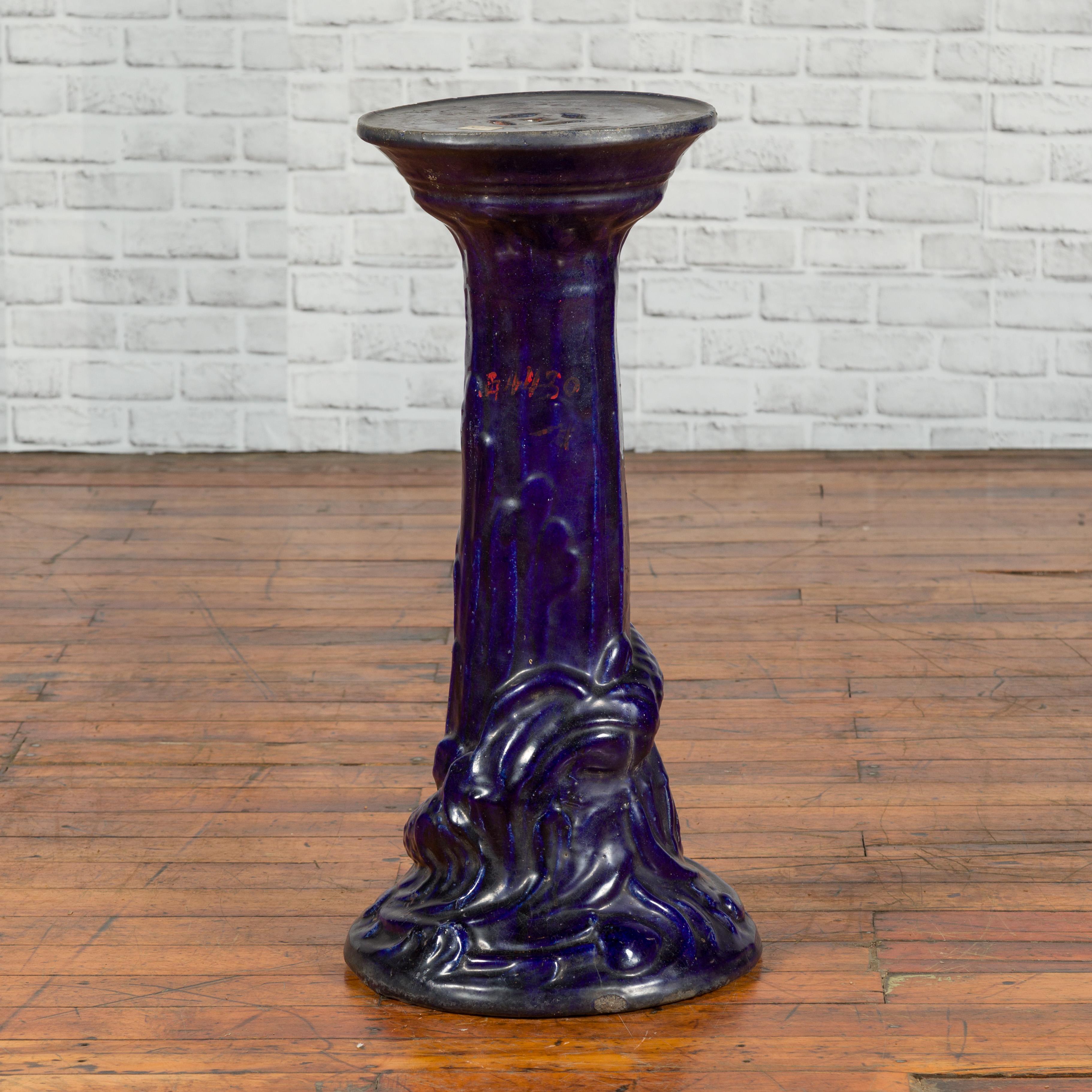 A Chinese antique dark blue glazed pedestal stand with raised motifs. Boasting a lovely dark blue glazed patina, this plant stand features a circular top pierced with small geometric openings, resting above a pedestal discreetly accented with raised