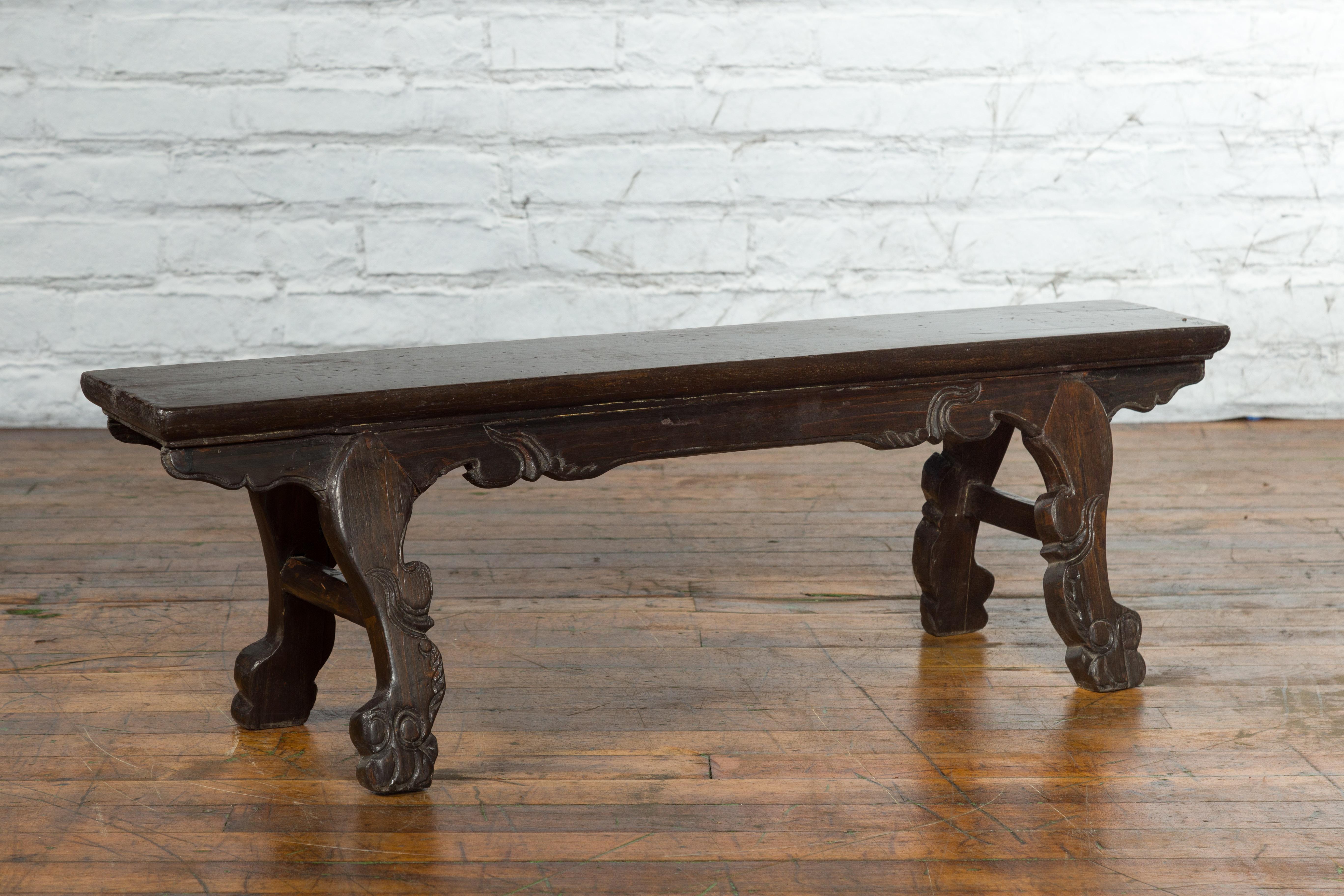 An antique Chinese low dark brown lacquered display table from the early 20th century with carved legs and apron. Created in China during the early years of the 20th century, this lacquered table features a narrow rectangular top sitting above an