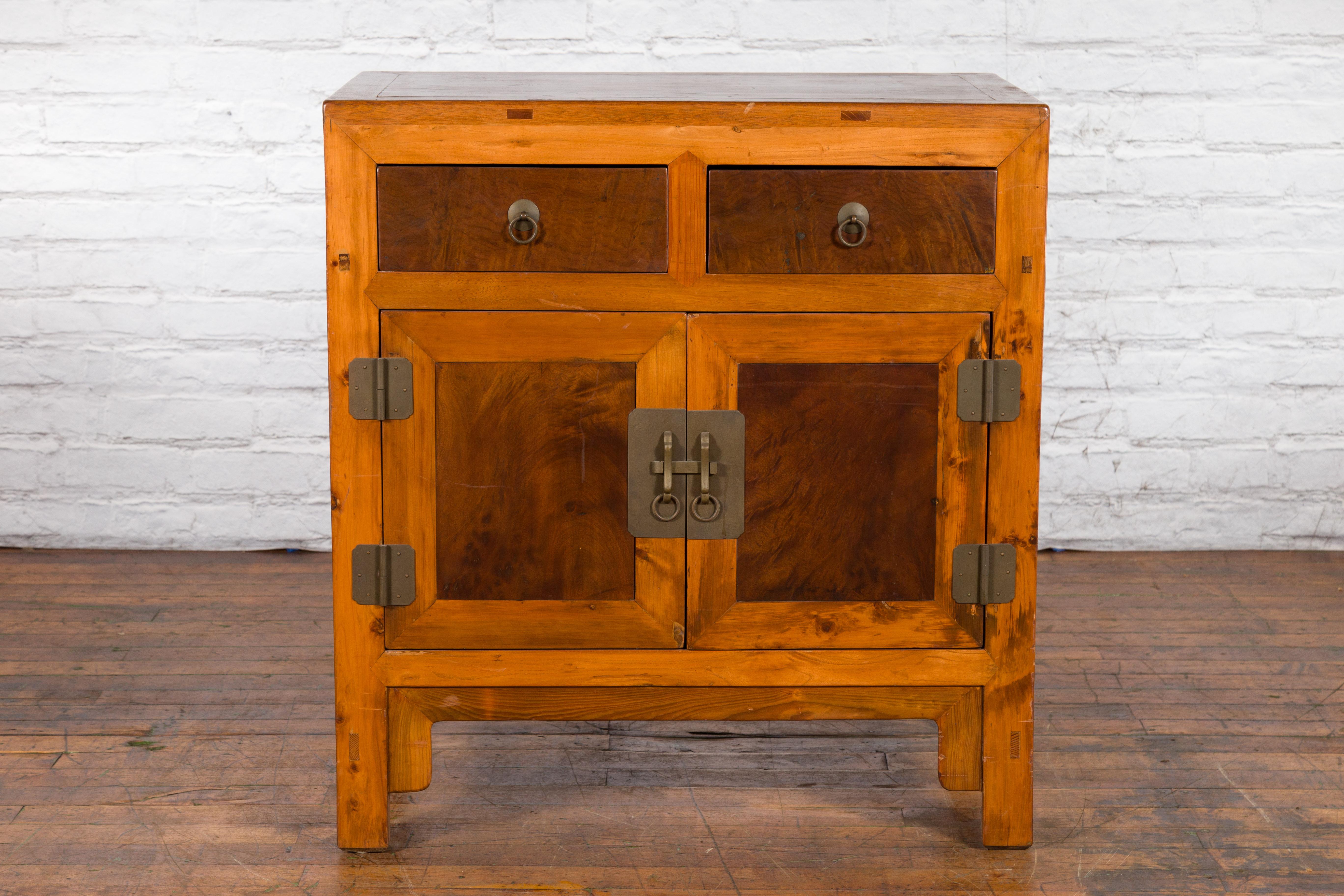An antique Chinese two-toned elm and burlwood side cabinet from the early 20th century, with two drawers and doors. Created in China during the early years of the 20th century, this side cabinet features a linear silhouette perfectly complimented by