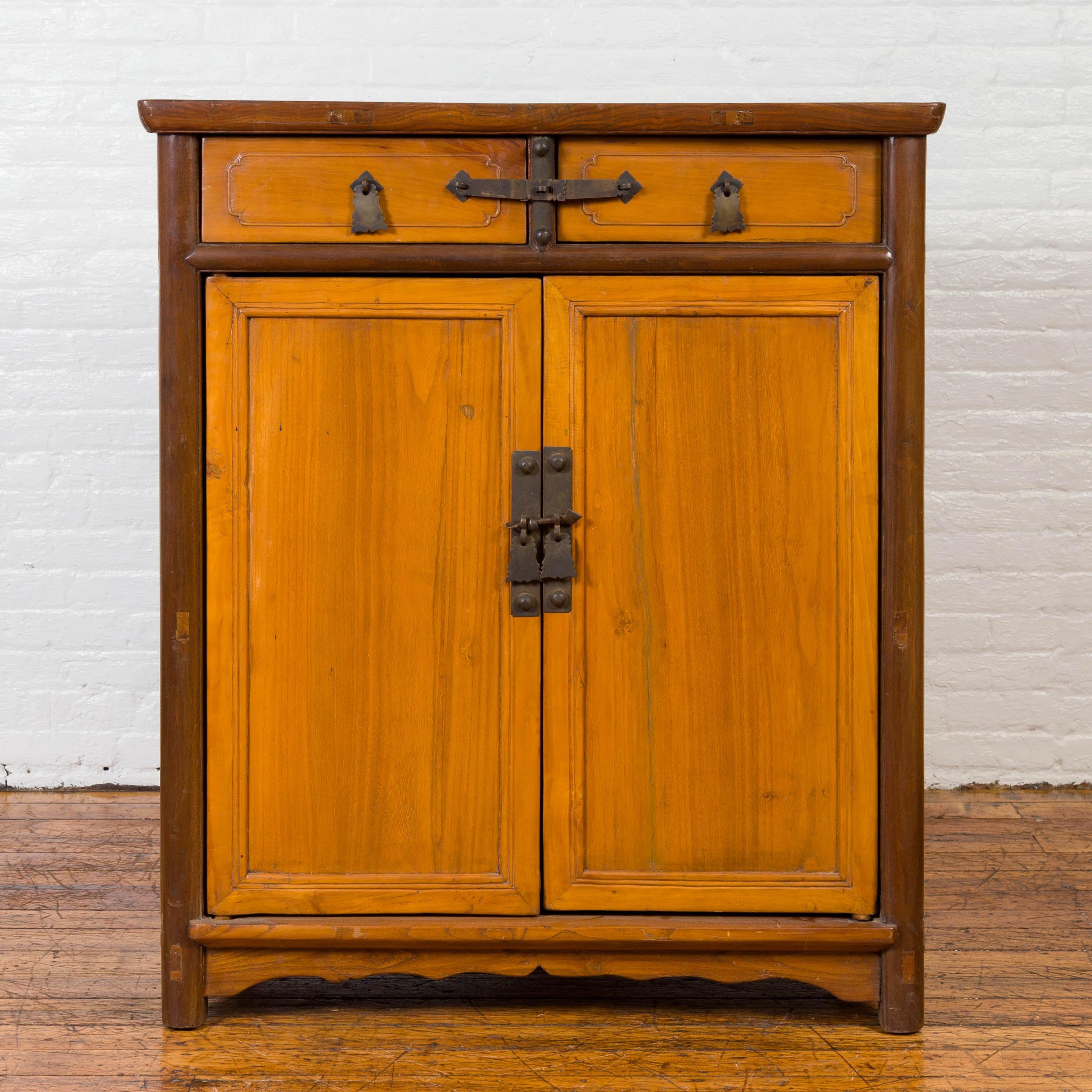 An antique Chinese elmwood two-toned cabinet from the early 20th century, with cut bronze hardware and brushed yellow hued patina. Attracting our attention with its clean lines and two-toned finish, this Chinese elm cabinet features a rectangular