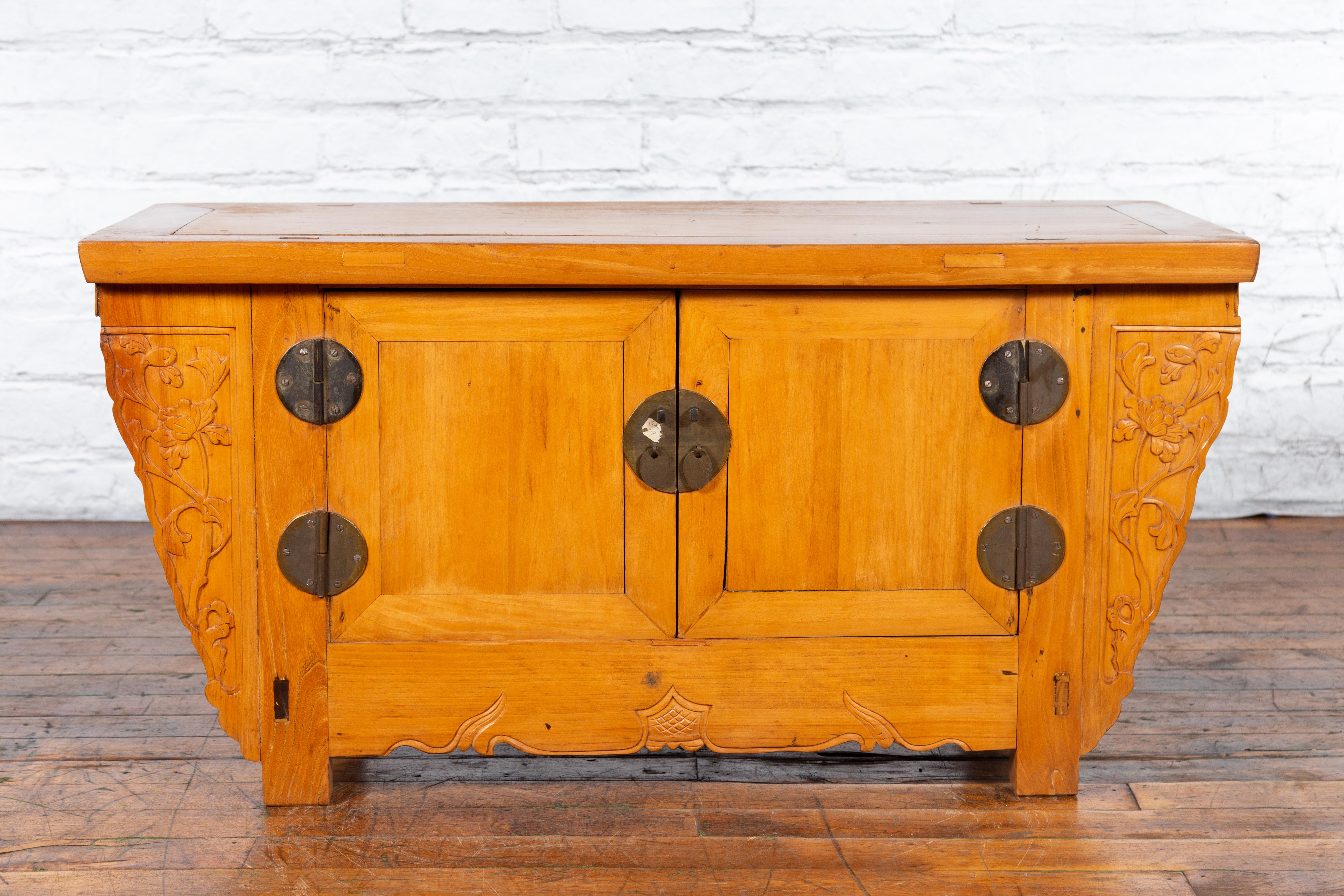 An antique Chinese elmwood sideboard from the early 20th century, with carved spandrels and bronze hardware. Created in China during the early years of the 20th century, this elm sideboard features a rectangular top with central board, sitting above