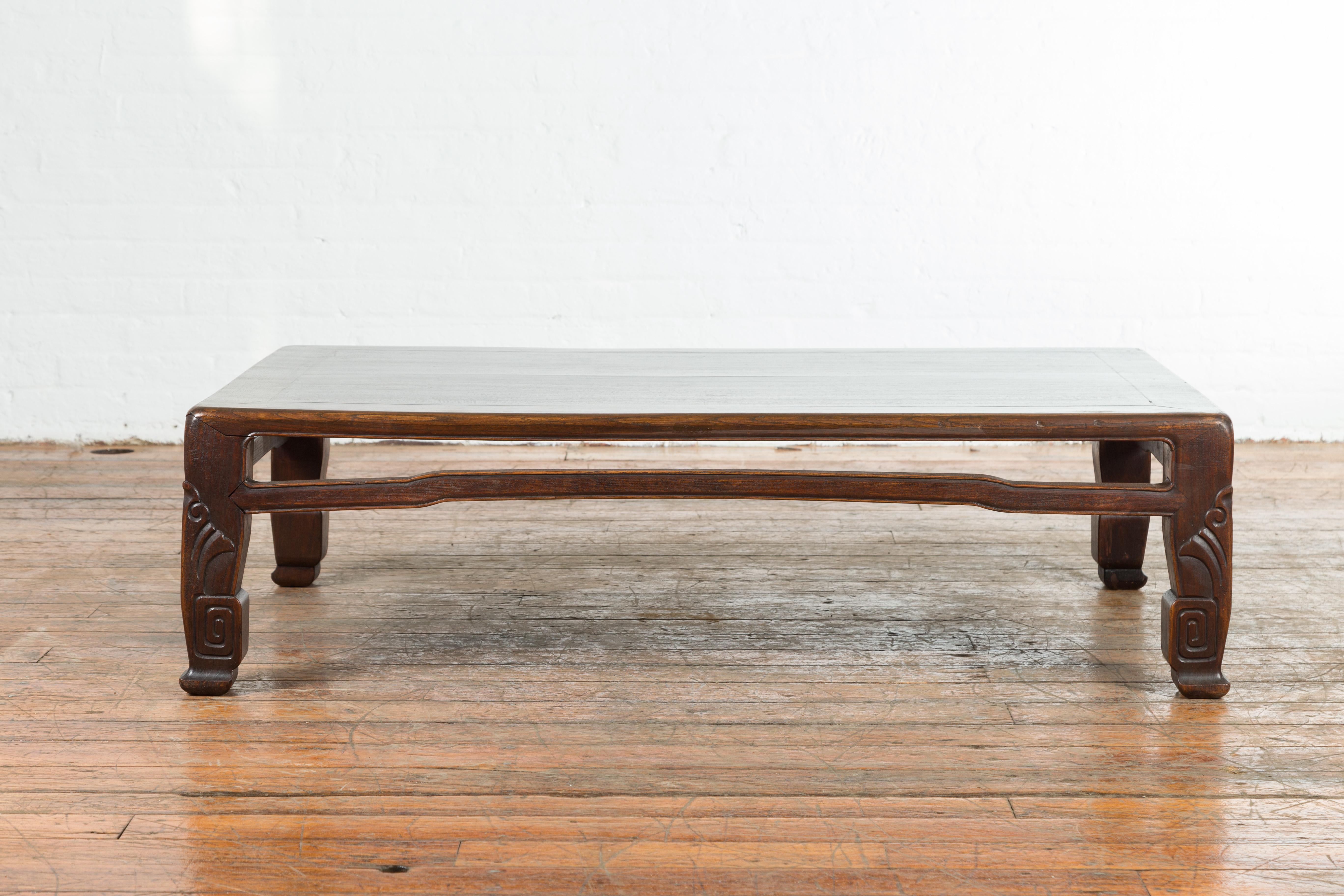 A Chinese antique elmwood coffee table from the early 20th century, with scrolling feet and humpback stretcher. Created in China during the early years of the 20th century, this elmwood coffee table features a rectangular planked top sitting above a