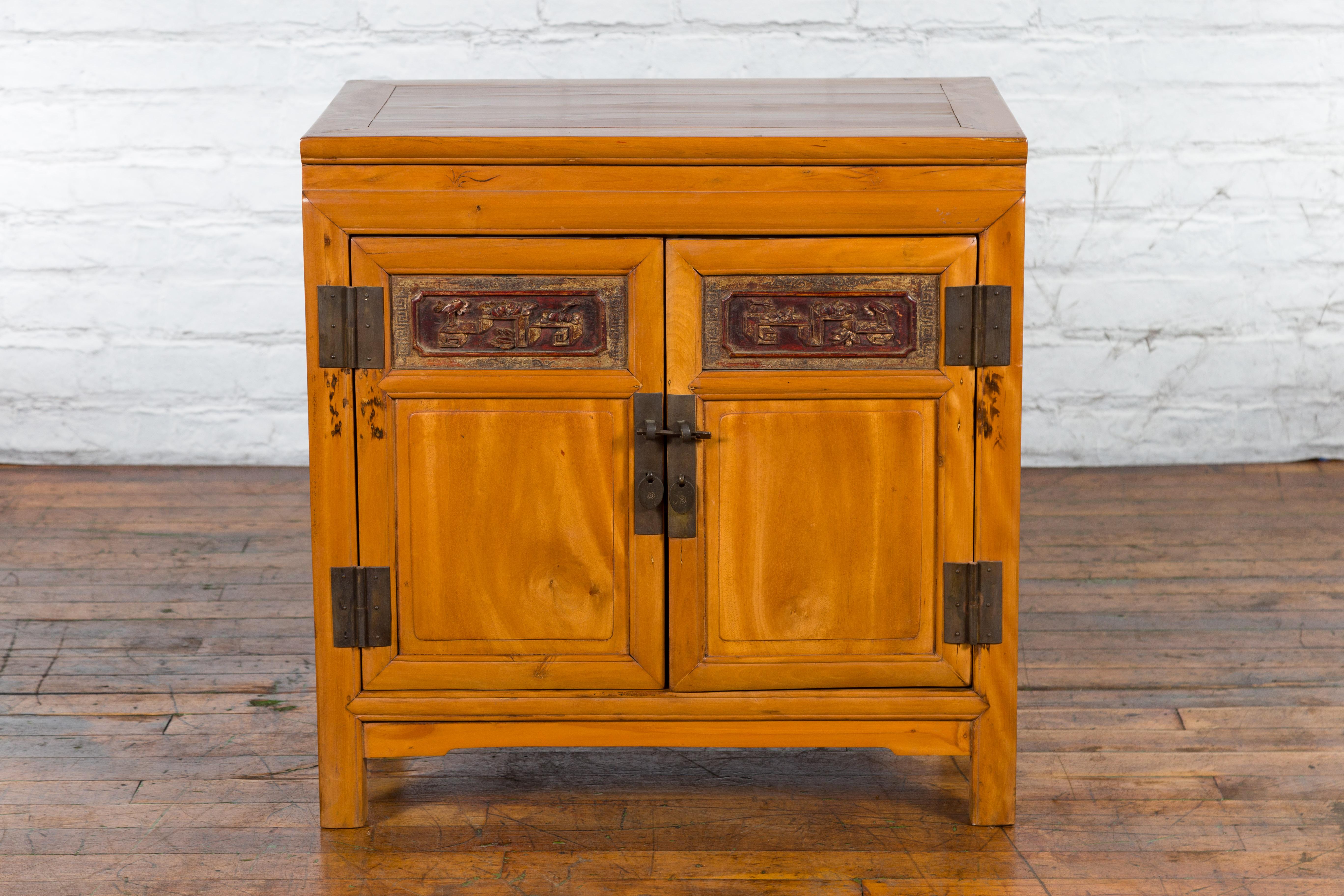 A Chinese elmwood side cabinet from the early 20th century with carved panels and hidden drawers. Created in China during the early years of the 20th century, this elmwood side cabinet features a rectangular top with central board, sitting above two
